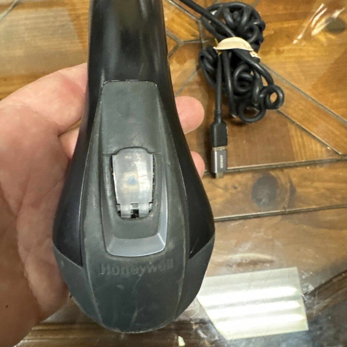 Used black Honeywell USB barcode scanner with coiled cable held in hand on wooden surface background
