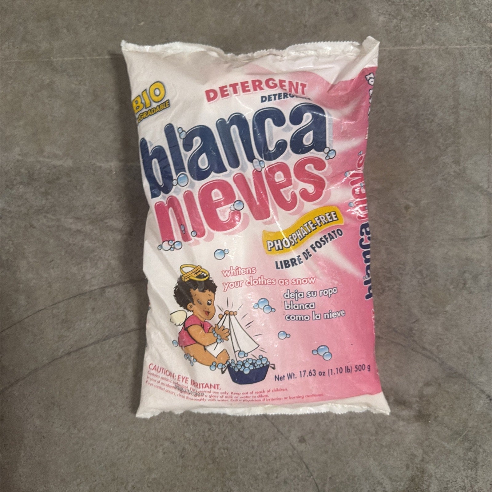 Bag of Blanca Nieves powdered detergent in pink and white packaging, highlighting phosphate-free formula and featuring an illustration of a child washing clothes in a basin of foamy water.