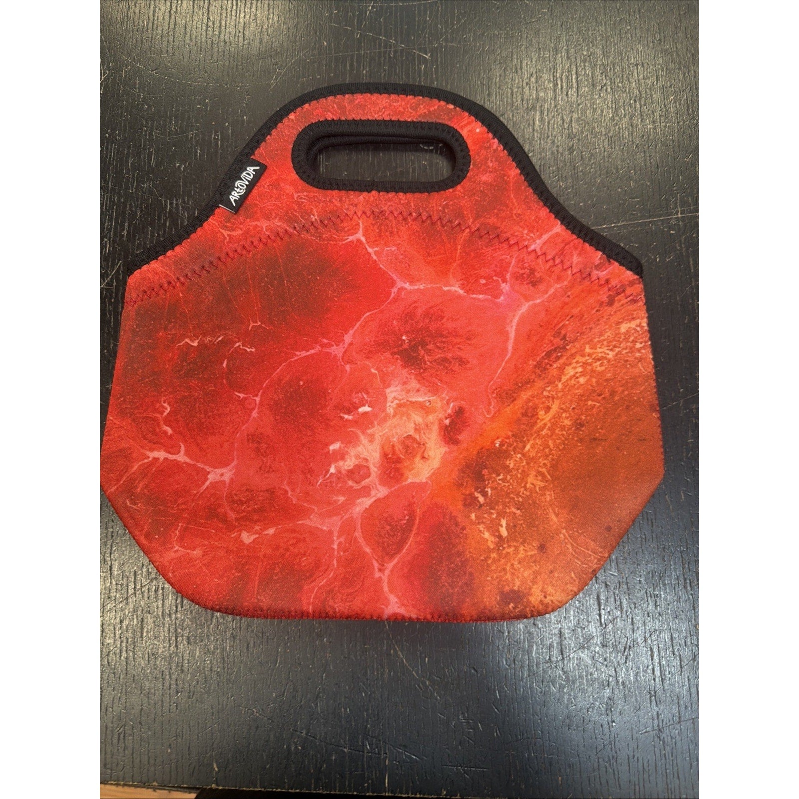 Red and orange insulated lunch tote with a soft neoprene texture and a built-in handle, placed on a dark wooden surface.