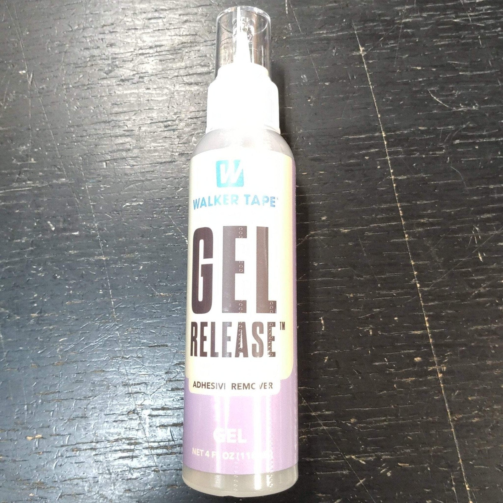 Clear plastic spray bottle of Walker Tape Gel Release adhesive remover with a white and lavender label, placed on a dark textured surface.