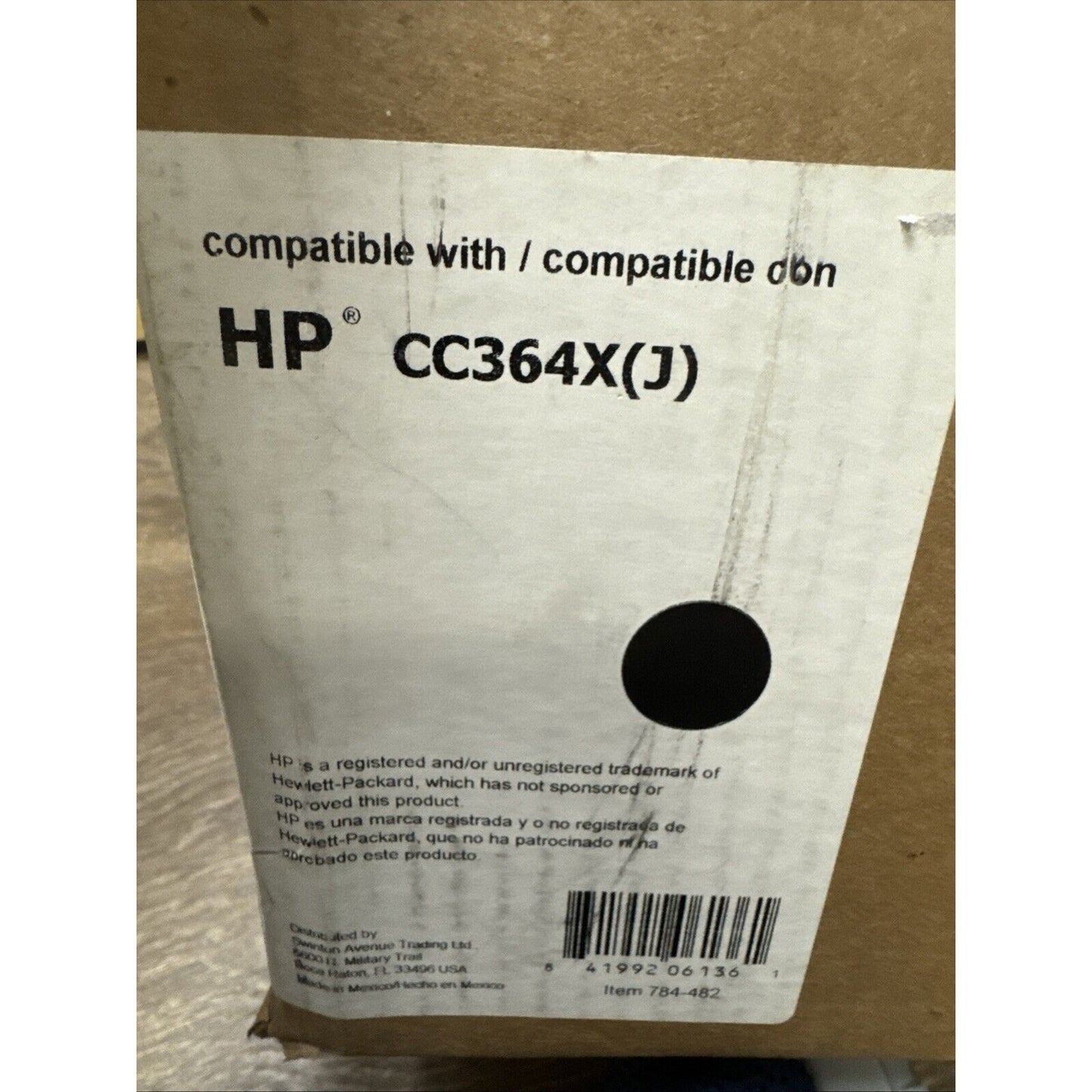 Brown cardboard box with a white label stating compatibility with HP CC364X(J) toner cartridge, including a circular black mark and a barcode at the bottom.