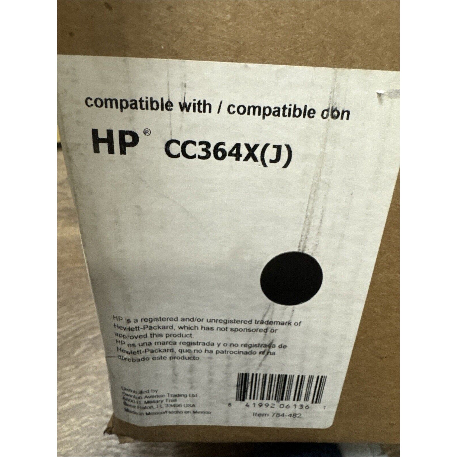 Brown cardboard box with a white label stating compatibility with HP CC364X(J) toner cartridge, including a circular black mark and a barcode at the bottom.