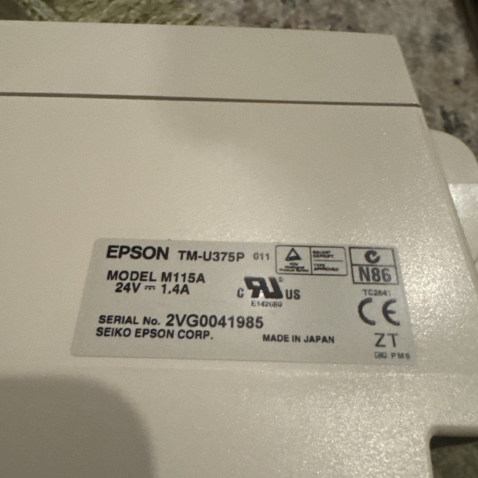 Close-up of EPSON TM-U375P Model M115A label showing serial number, power specifications, and certification marks on beige printer casing