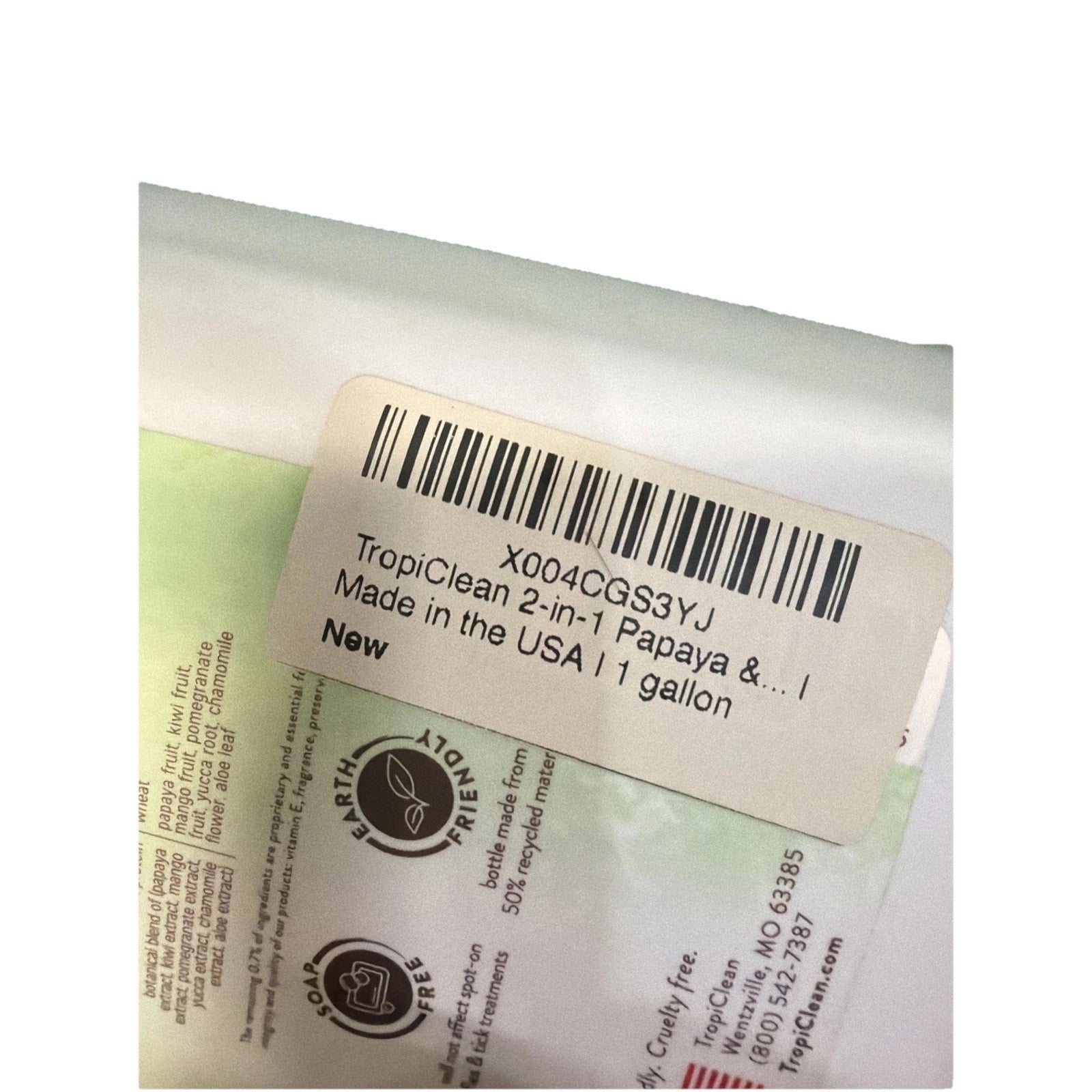 Close-up of a white product label on packaging featuring a barcode, text indicating a 1-gallon TropiClean 2-in-1 Papaya product made in the USA, and eco-friendly icons on a light green and white background.