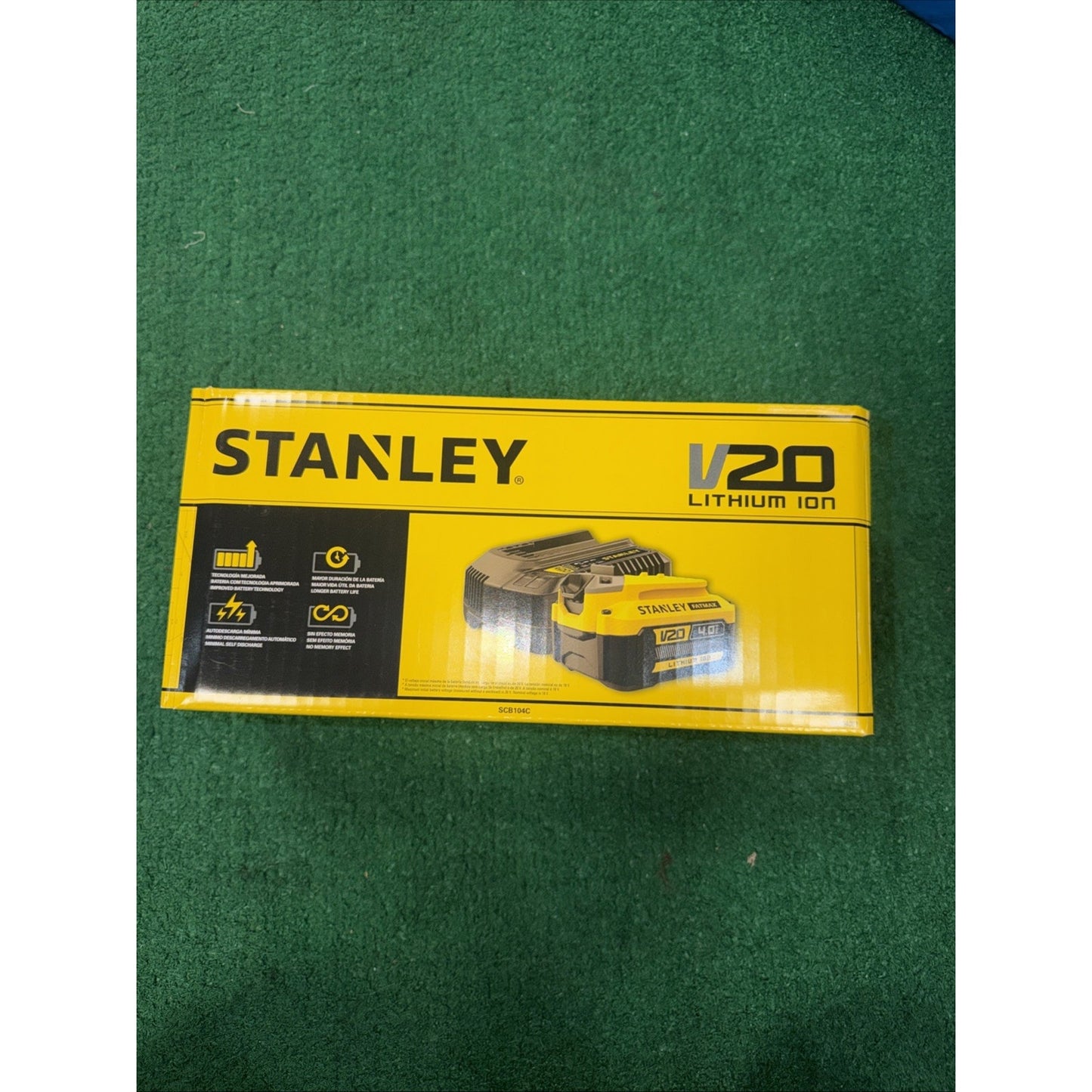 Yellow and black Stanley V20 Lithium Ion battery packaging box displayed on a green carpet, featuring product image and key performance icons on the front panel.