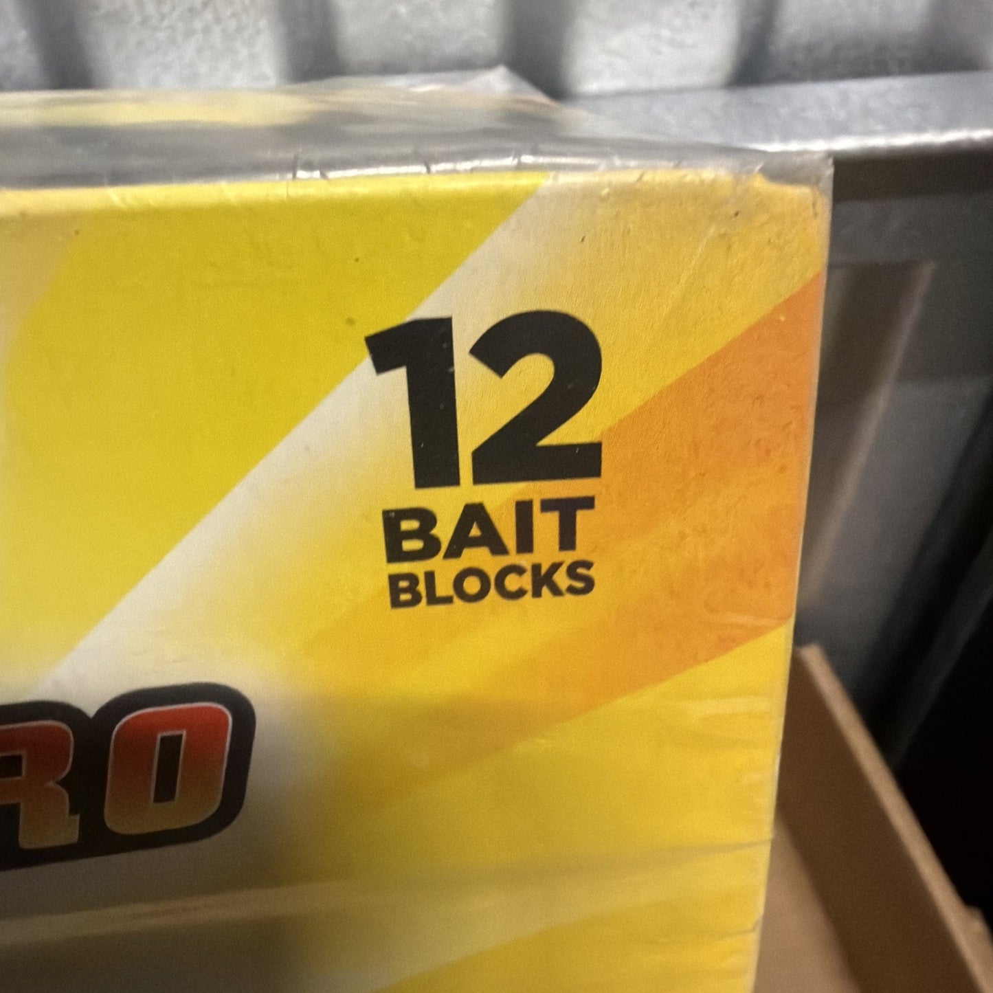 Corner of a yellow and orange box displaying bold black text indicating the package contains 12 bait blocks, with part of a black and red logo visible on the left side.