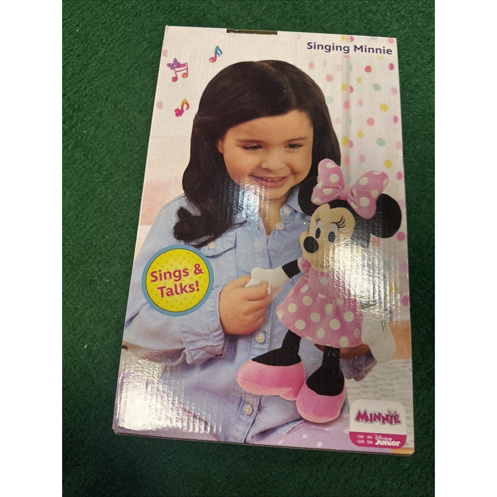 Box packaging of Disney Minnie Mouse Happy Helpers 12 inch singing plush doll held by smiling child with pink polka dot dress
