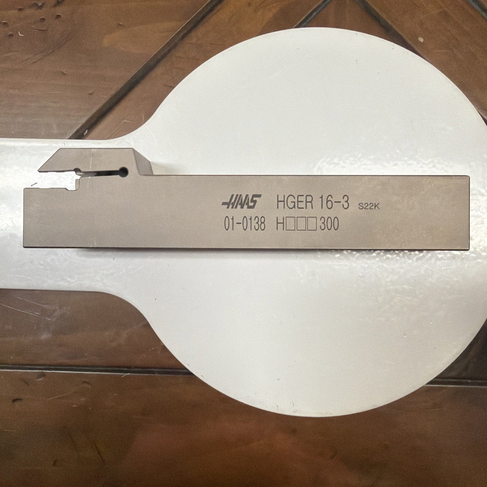 Rectangular metal cutting tool with engraved text including the brand name, model number, and specifications, resting on a wooden surface.