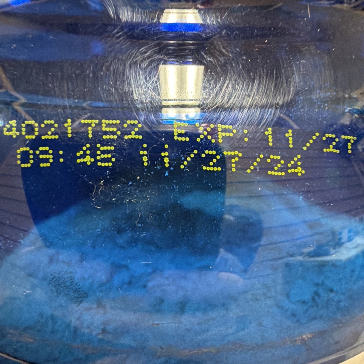 Close-up of a blue plastic container showing a yellow printed expiration date of 11/27 and a timestamp of 08:46 on the surface.