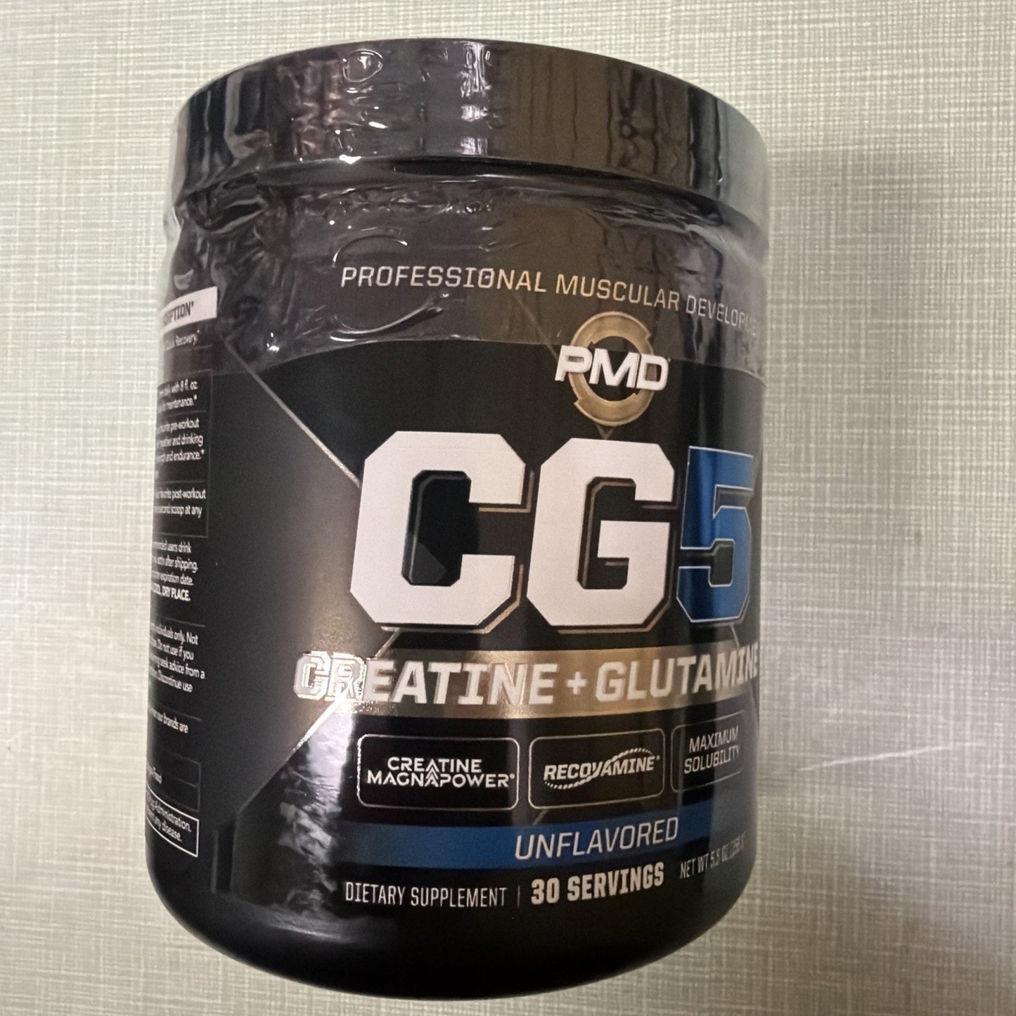 Black plastic container of CG5 dietary supplement featuring creatine and glutamine with branding details emphasizing creatine magnapower, recovamine, and maximum solubility, labeled unflavored and containing 30 servings.
