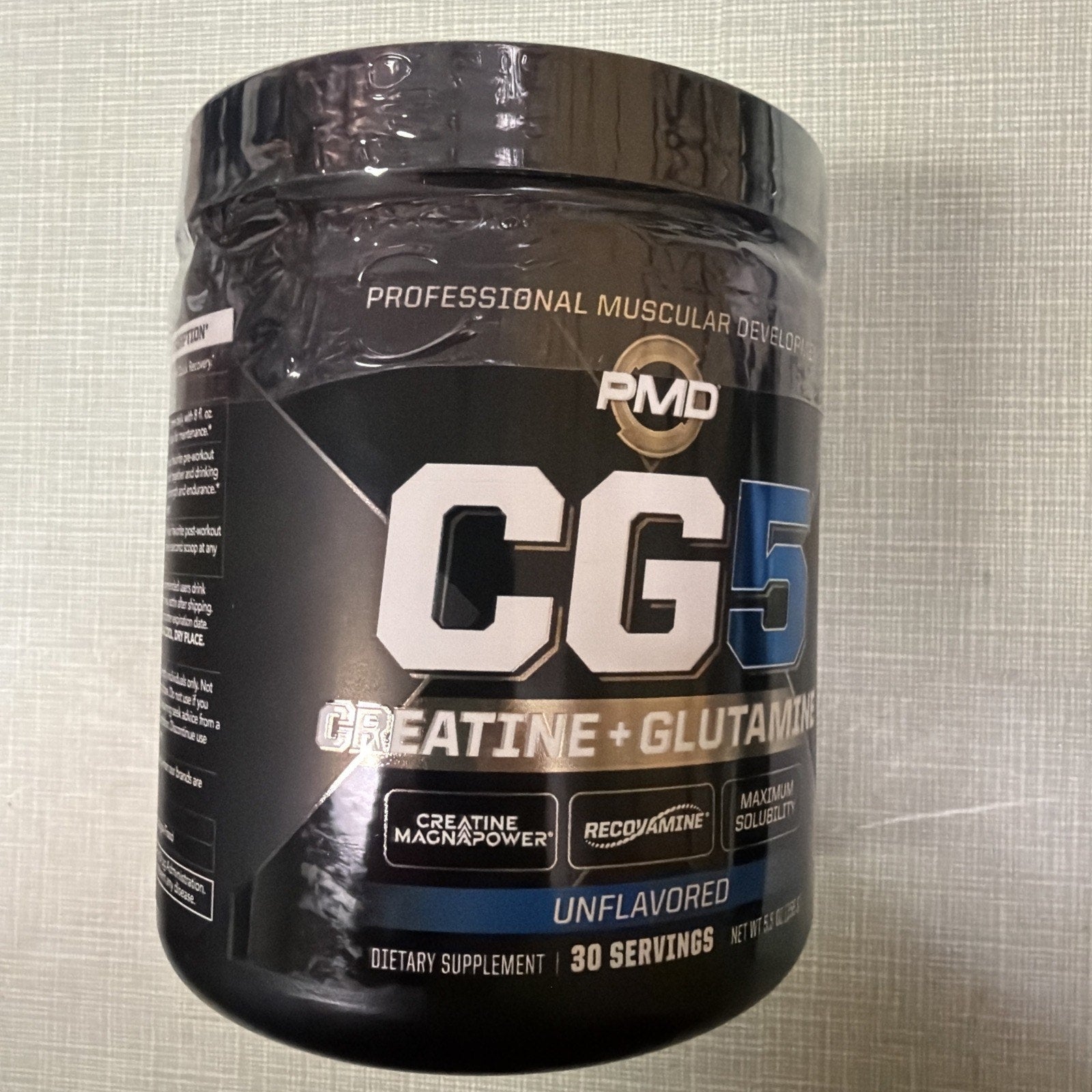 Black plastic container of CG5 dietary supplement featuring creatine and glutamine with branding details emphasizing creatine magnapower, recovamine, and maximum solubility, labeled unflavored and containing 30 servings.