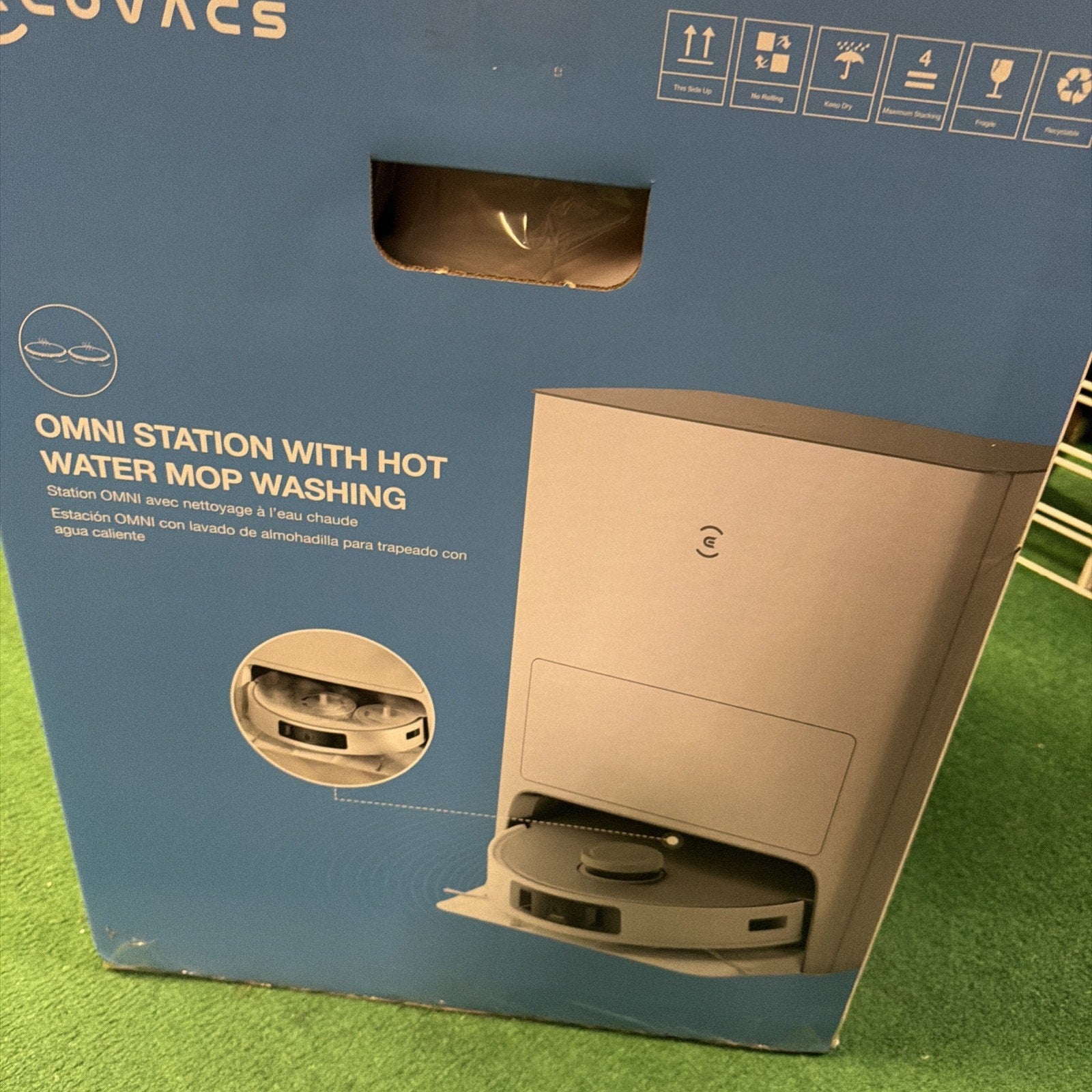 Blue packaging box featuring an image of a robot vacuum cleaning station with hot water mop washing function, including text and handling symbols on the top right corner.