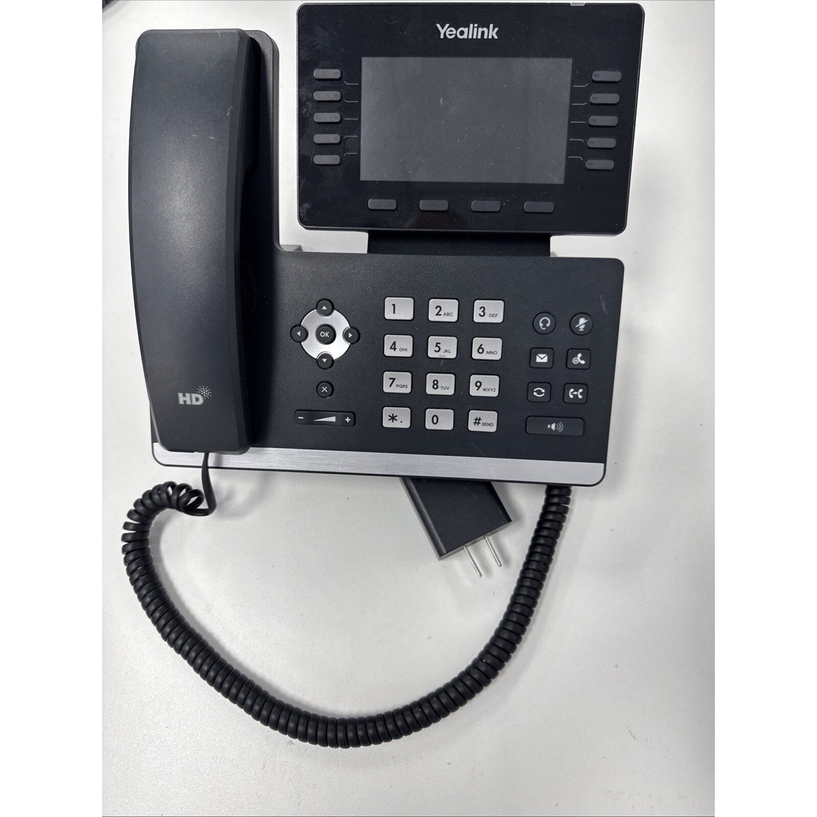 Black Yealink office desk phone featuring a large screen, multiple function buttons, numeric keypad, and a coiled handset cord on a white surface.