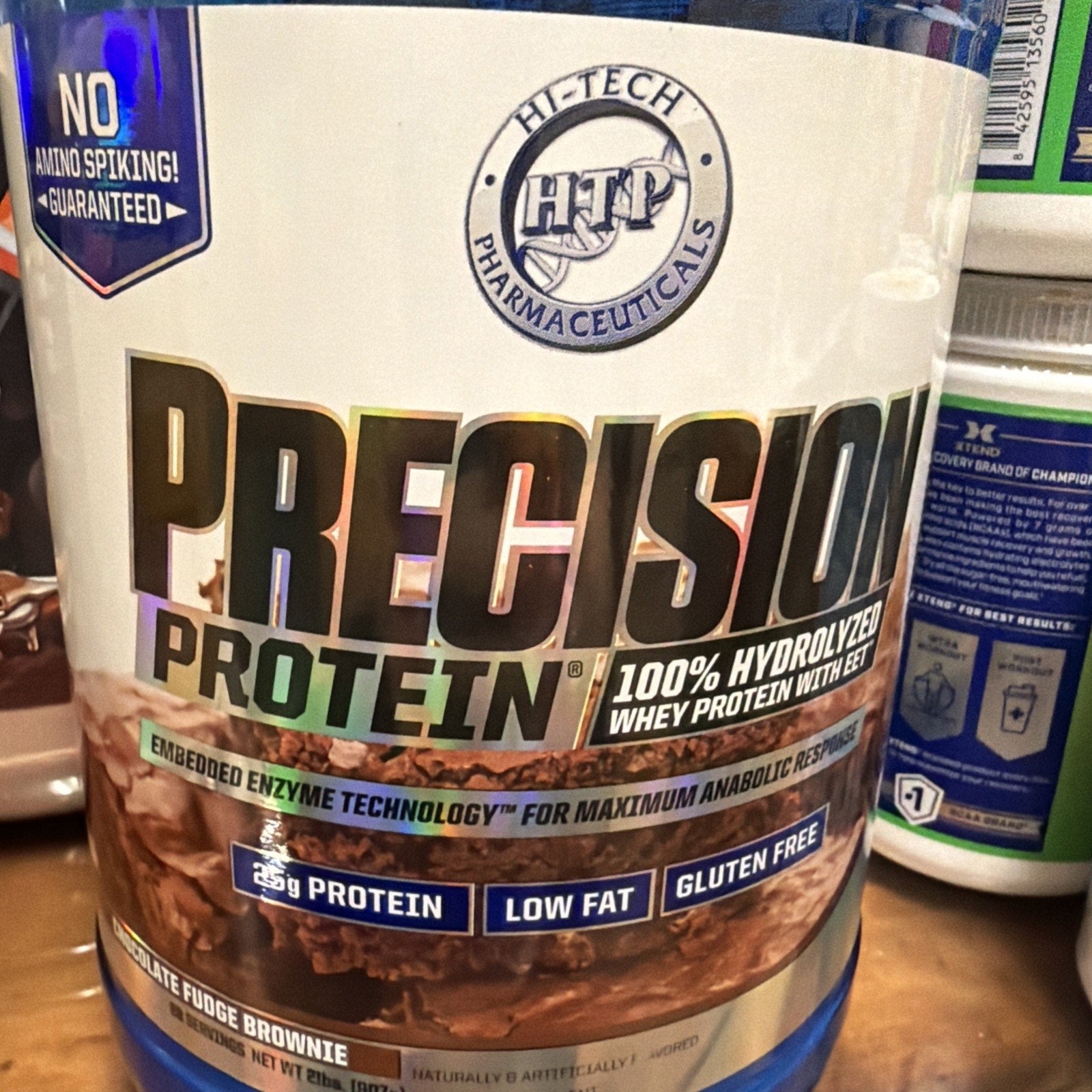 Container of Hi-Tech Pharmaceuticals Precision Protein whey protein powder in chocolate fudge brownie flavor, featuring 25 grams of protein, low fat, gluten-free, and enzyme technology for anabolic response.