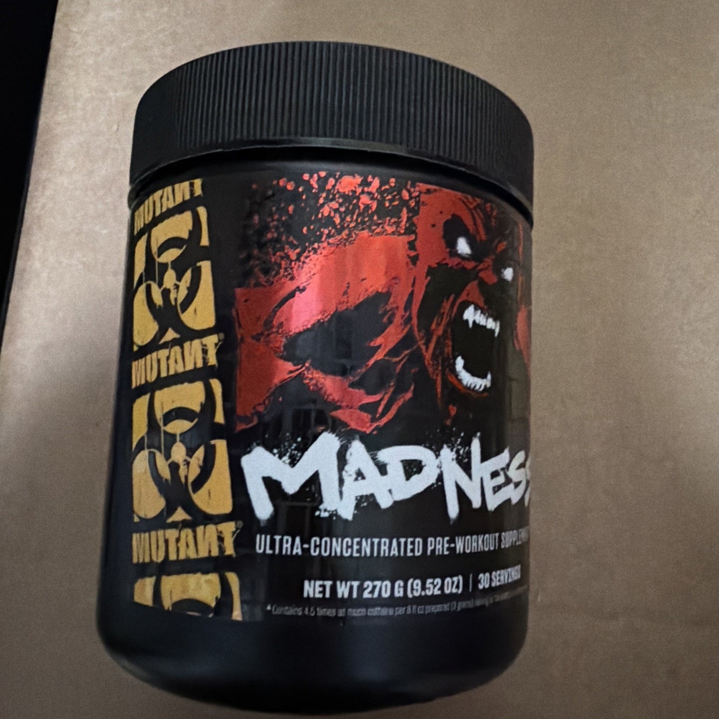 Matte black plastic container of Mutant Madness pre-workout supplement featuring aggressive red and black graphic of a roaring creature and bold white and yellow text on the label.