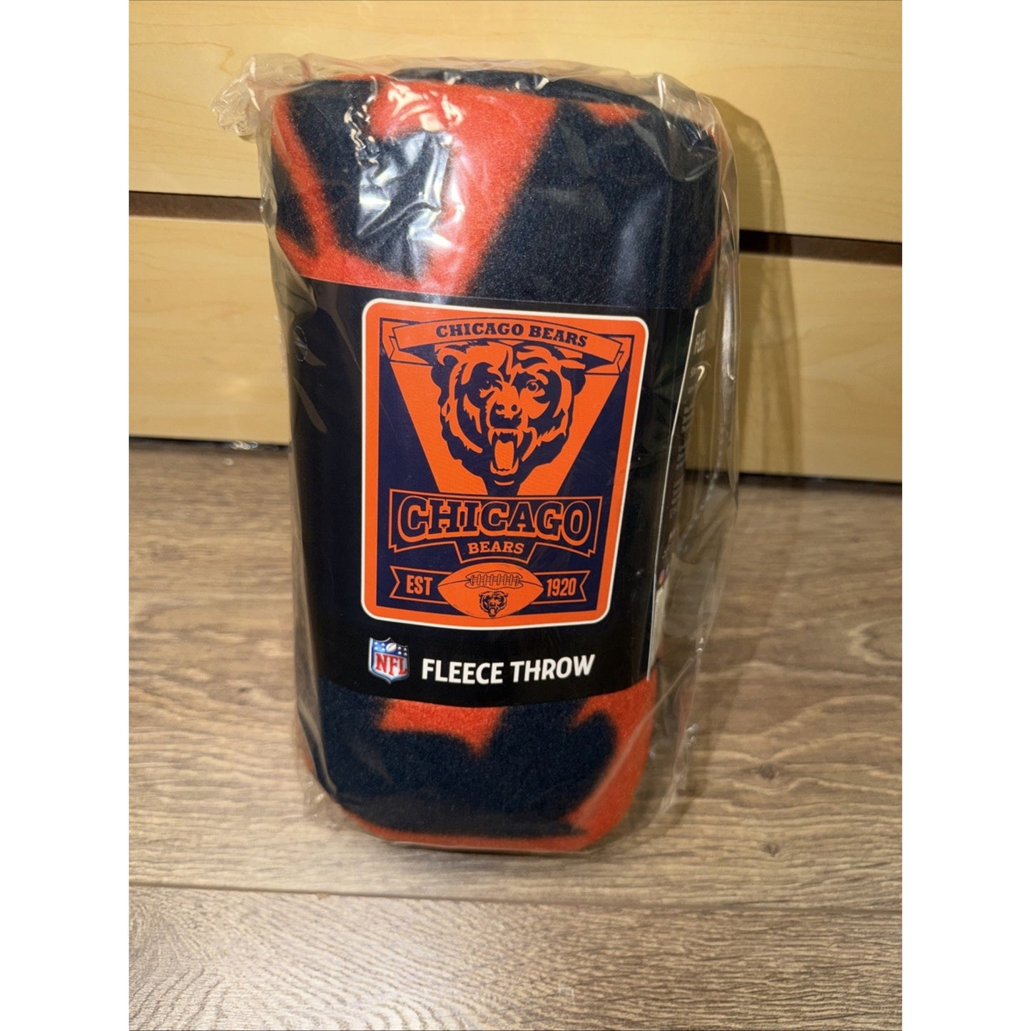 Rolled fleece throw blanket featuring the Chicago Bears logo and team colors, wrapped in clear plastic packaging on a wooden surface.