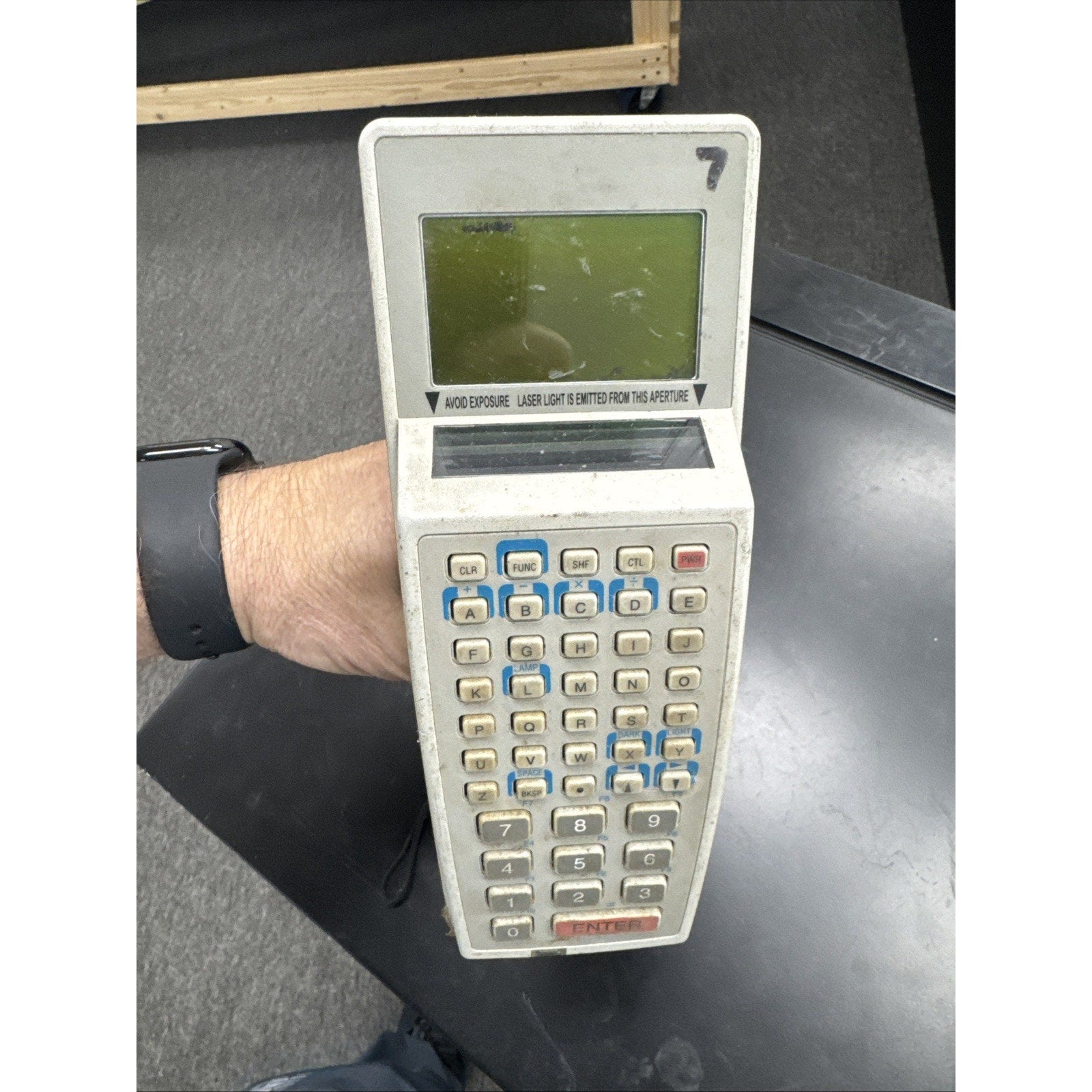 Handheld Symbol barcode scanner with integrated keypad and small screen held by person wearing black wristband