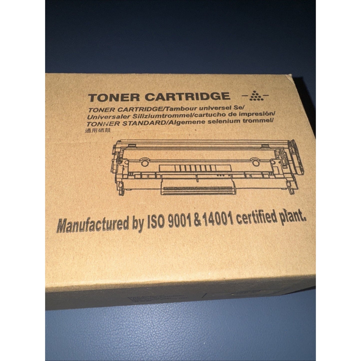 Brown cardboard box showing illustration and multilingual text for a universal toner cartridge, with certification stating ISO 9001 and 14001 compliance printed on surface.