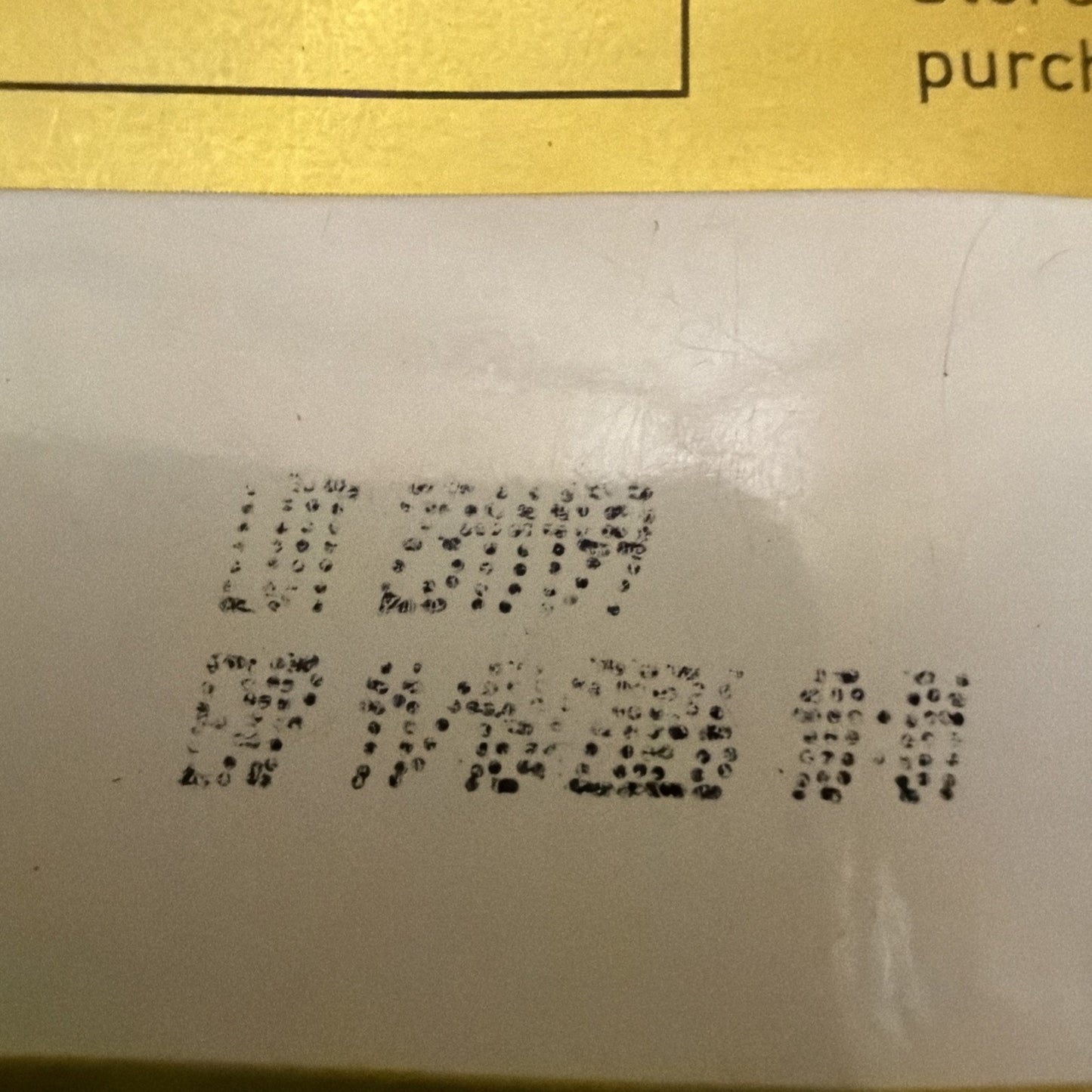 Close-up of a printed expiration or batch code in black ink on a white surface beneath a yellow section of packaging, with partially visible text above.