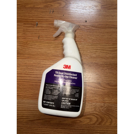 White plastic spray bottle of 3M TB Quat Disinfectant Ready-to-Use Cleaner placed on a wooden surface with a purple and black label.
