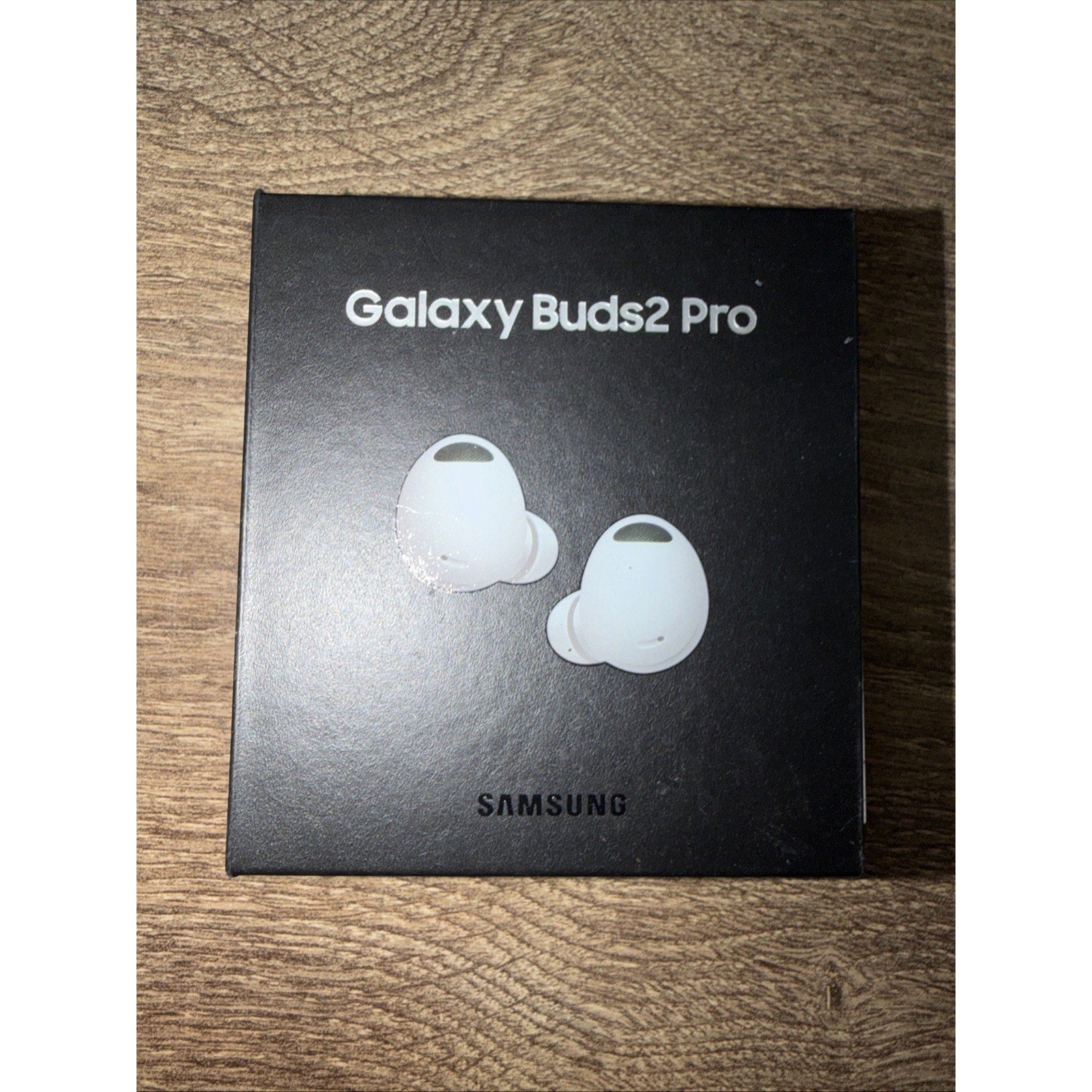 Black Samsung Galaxy Buds2 Pro box with silver text and an image of two white wireless earbuds, set on a wooden surface.