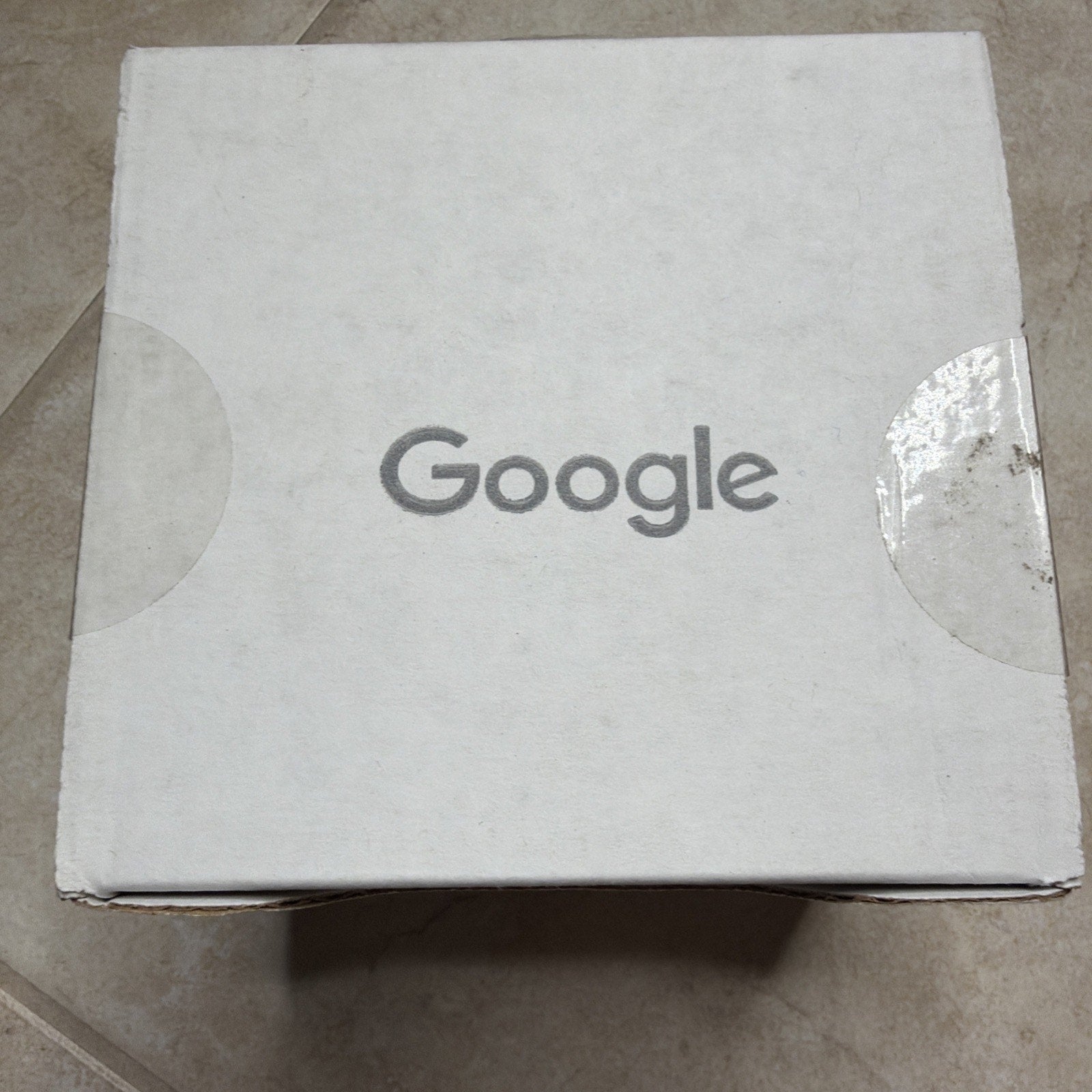 White cardboard box with the Google logo printed in gray on the top, showing slightly worn edges and a small dirt mark near the right semi-circular tab.