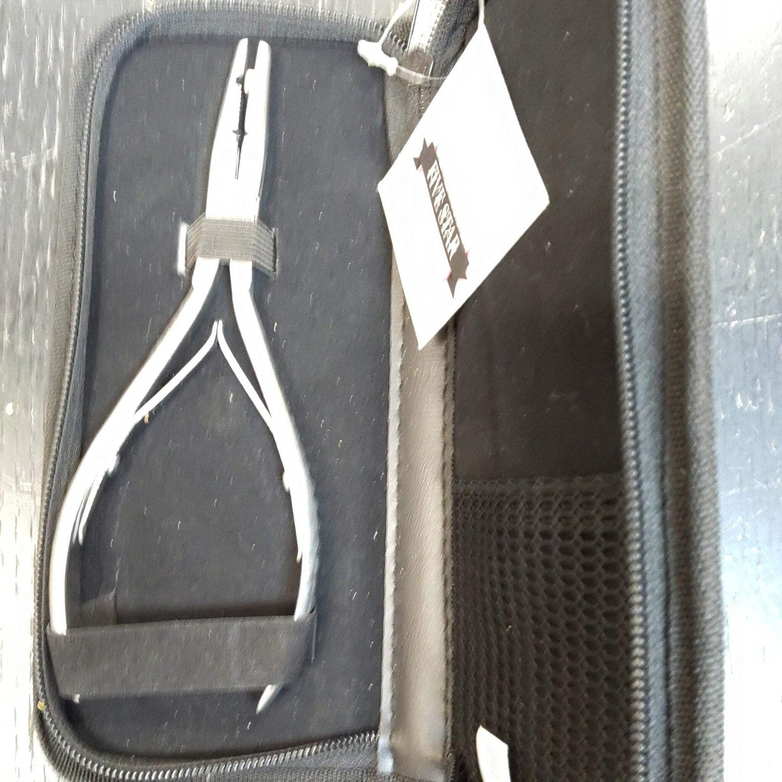 Silver metal nail nipper with black grip handles secured inside a black zippered carrying case featuring a mesh pocket and a white tag attached.