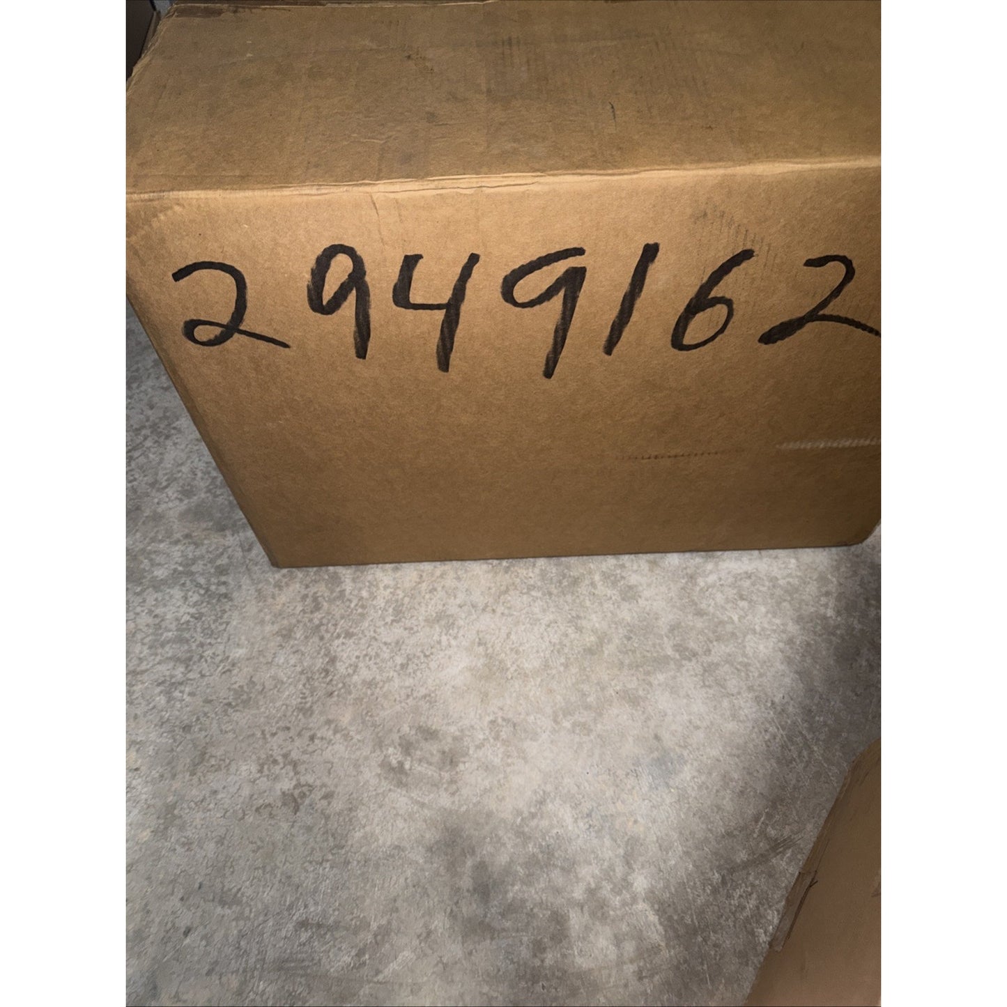 Brown cardboard box placed on a light gray textured concrete floor with the handwritten number 2949162 marked in black ink on the side.