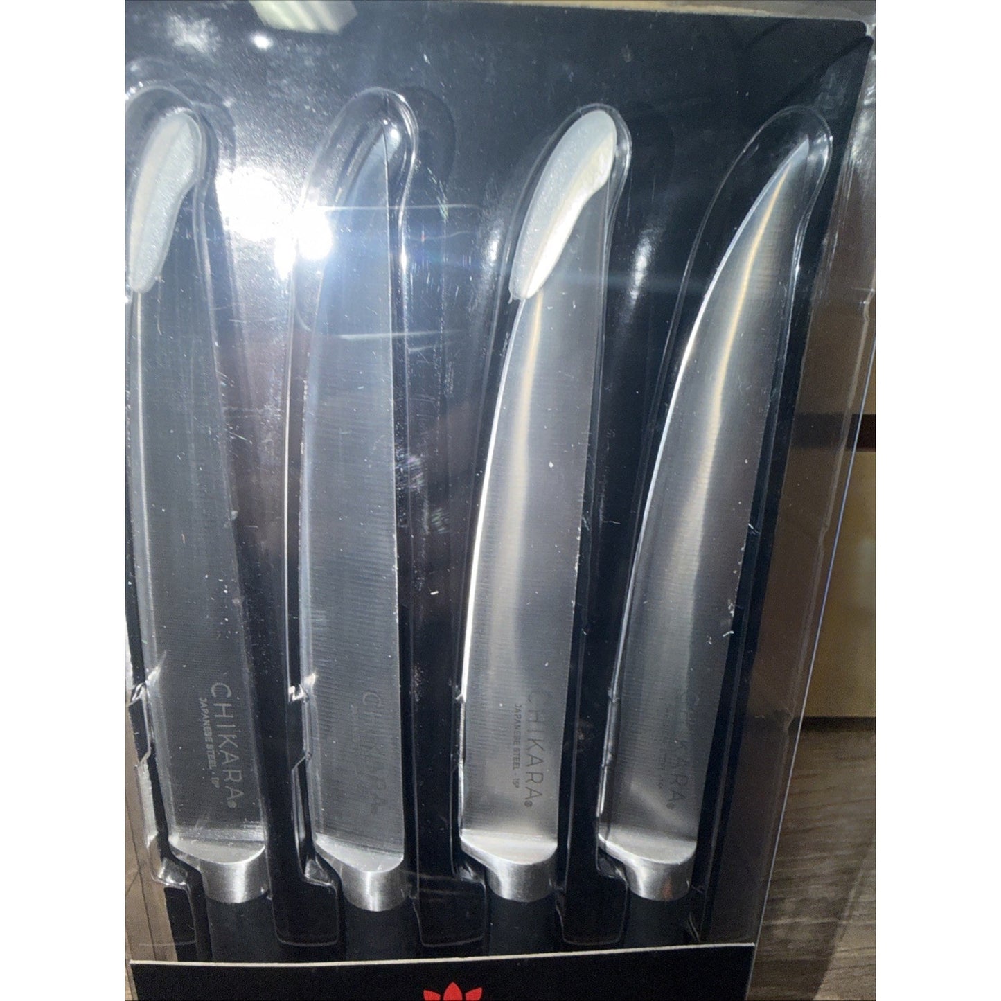 Set of four stainless steel kitchen knives with smooth, curved blades and ergonomic handles, displayed in a black plastic holder inside clear packaging.