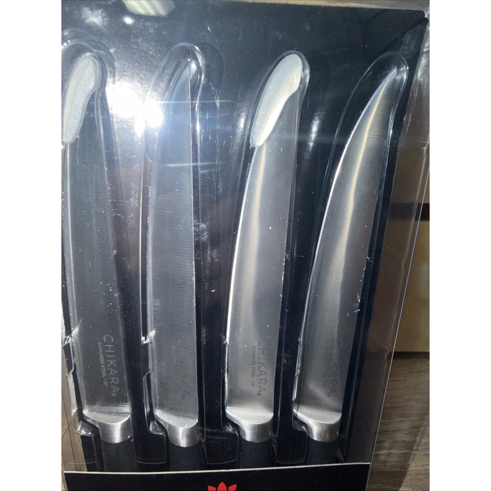 Set of four stainless steel kitchen knives with smooth, curved blades and ergonomic handles, displayed in a black plastic holder inside clear packaging.