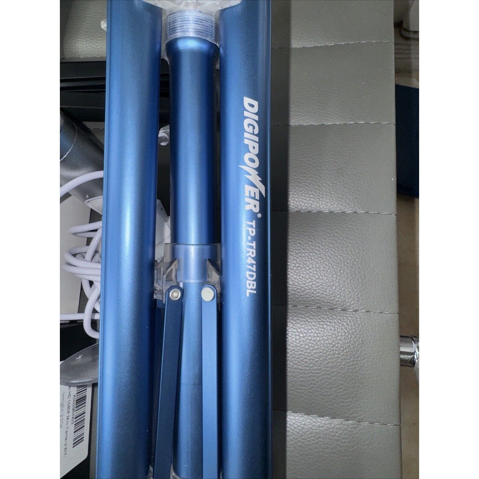 Blue Digipower TP-TR47DBL tripod legs folded and placed on a gray padded surface with cords nearby