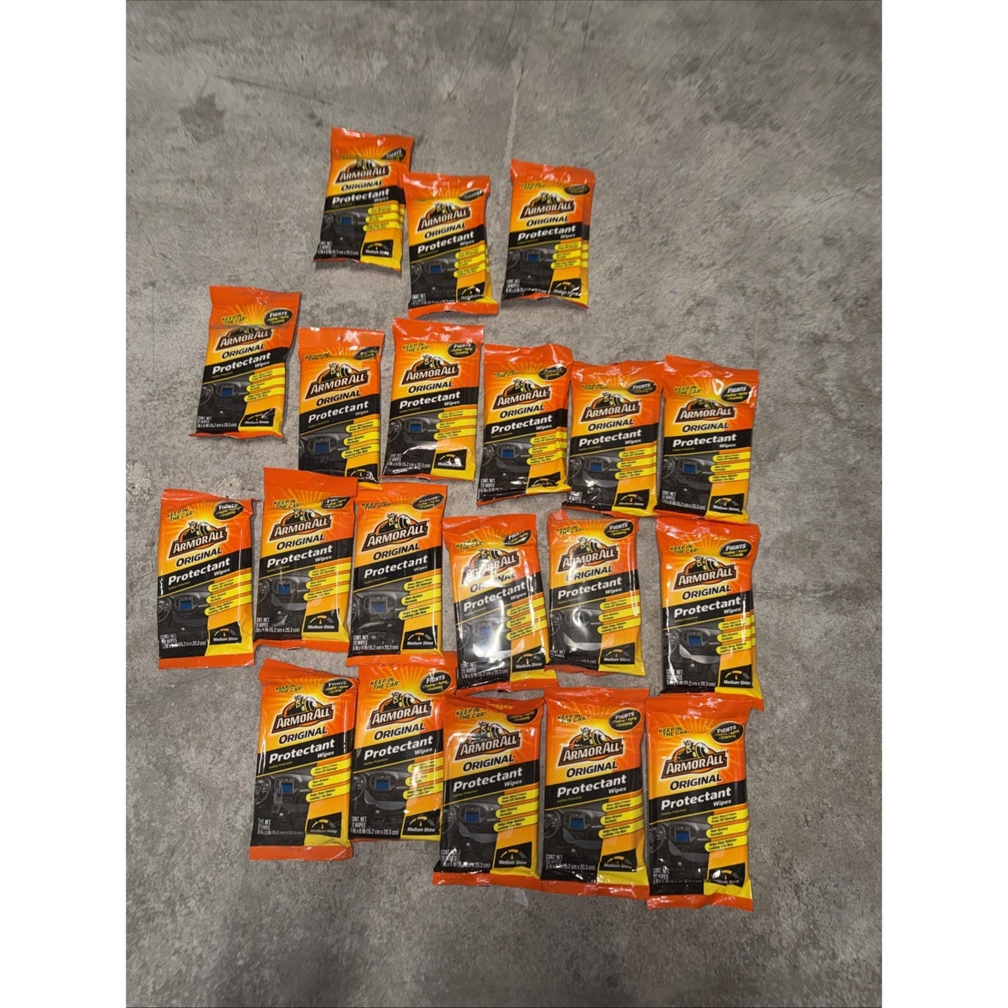 Multiple individual packets of Armor All Original Protectant, arranged on a concrete surface, with orange, yellow, and black packaging featuring product branding and usage information.