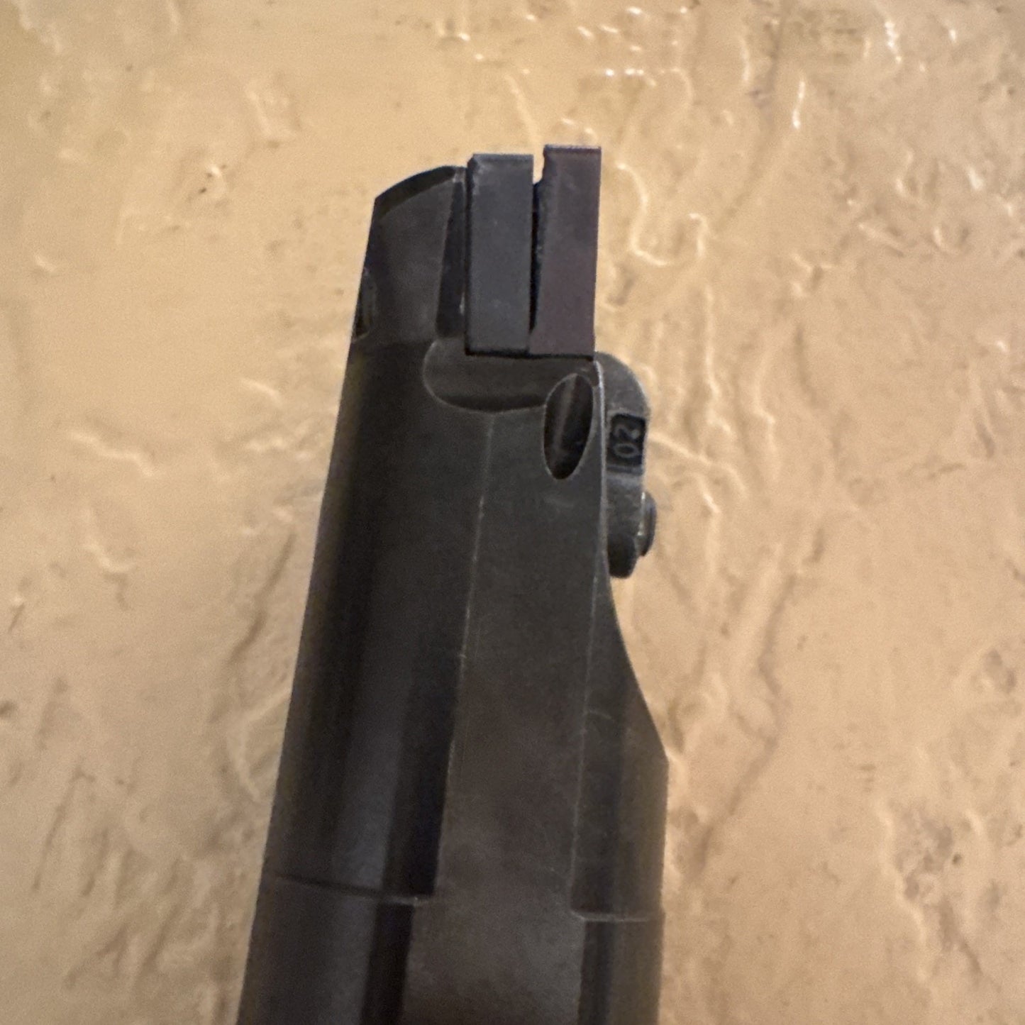 Close-up view of a black metal tool tip featuring two parallel rectangular cutting edges with a small screw on the side, set against a textured beige background.