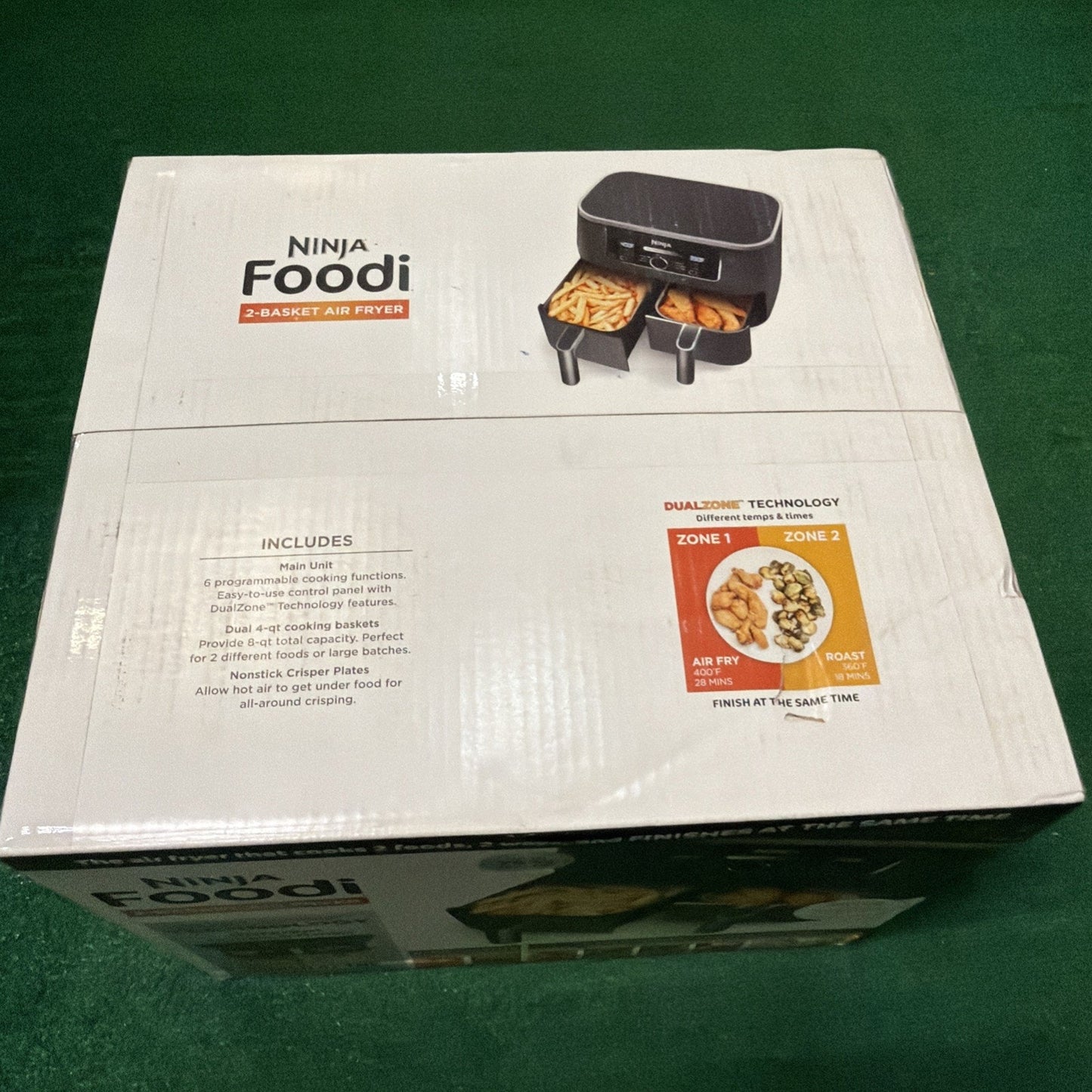 White cardboard box packaging for a Ninja Foodi 2-basket air fryer, showing an image of the appliance with two baskets containing fries and vegetables, along with text highlighting dual-zone cooking technology.