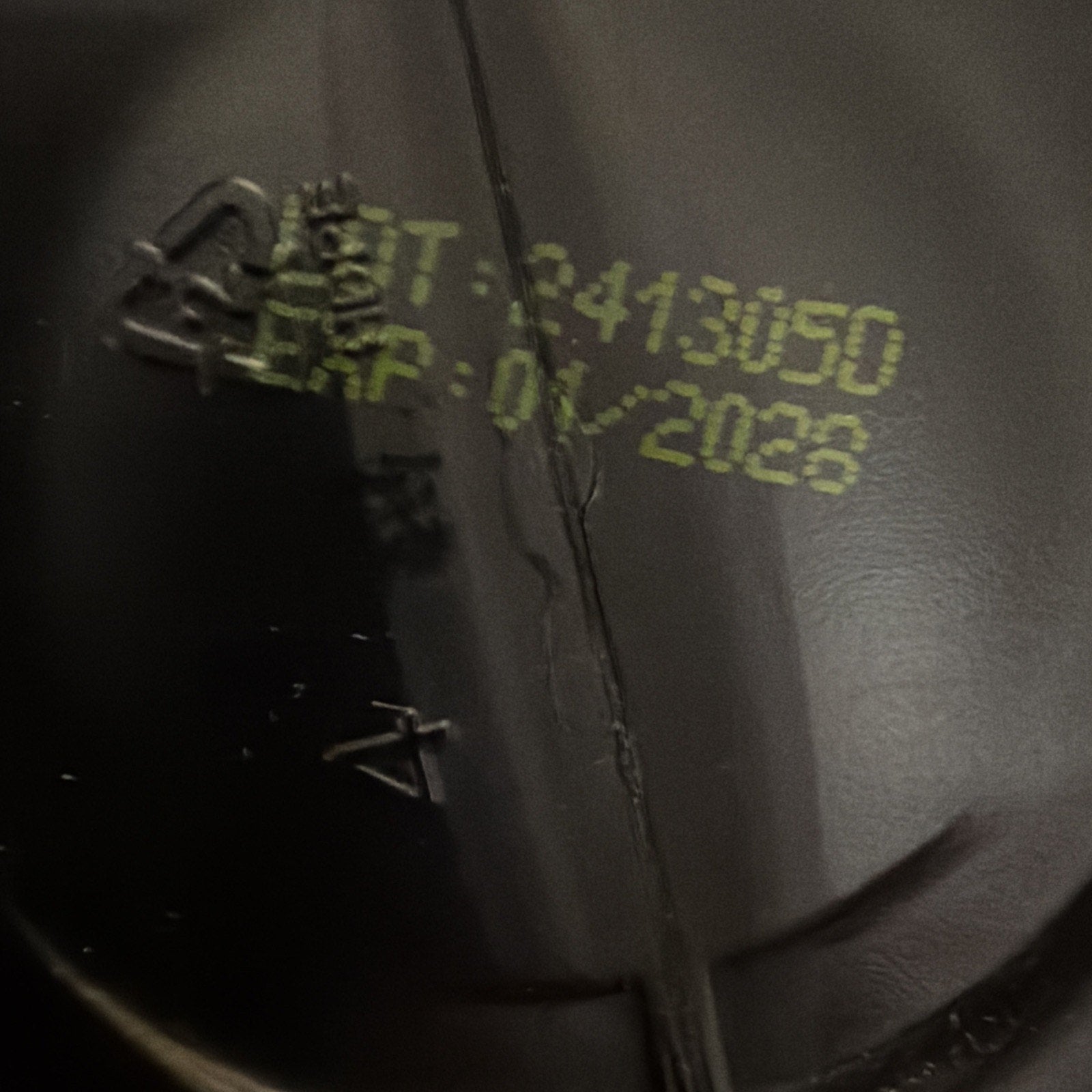 Close-up of a black plastic surface with yellow printed batch number "2413090" and expiration date "01/2028" on a textured background.