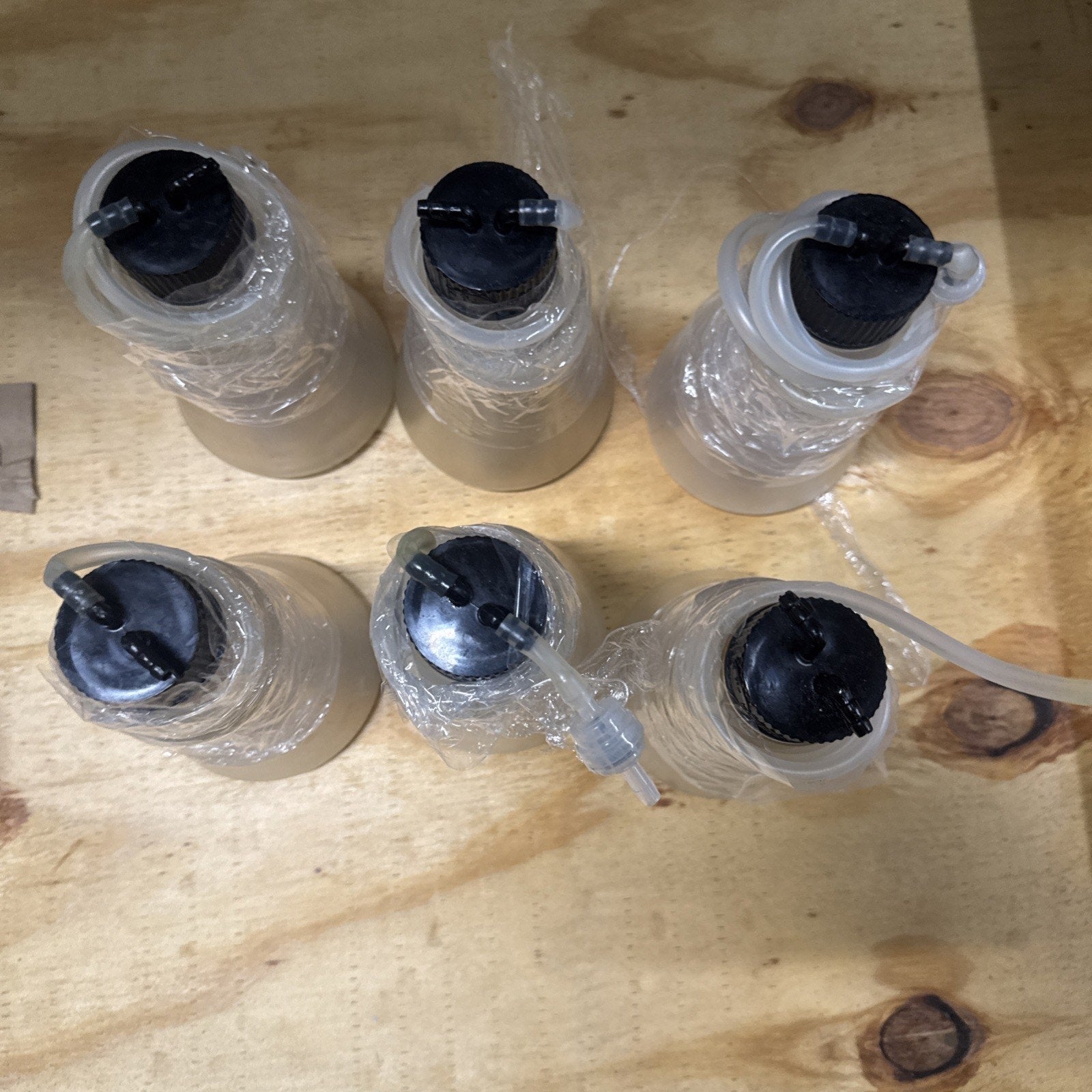 Set of six oxygen bar scent bottles with black caps and clear tubing on wooden surface wrapped in plastic wrap