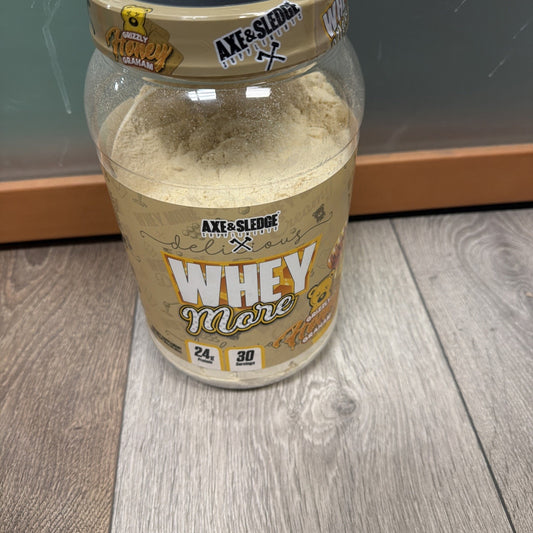Open container of Axe & Sledge Whey More protein powder in peanut butter flavor, showing light beige powder inside and label indicating 24 grams of protein and 30 servings.