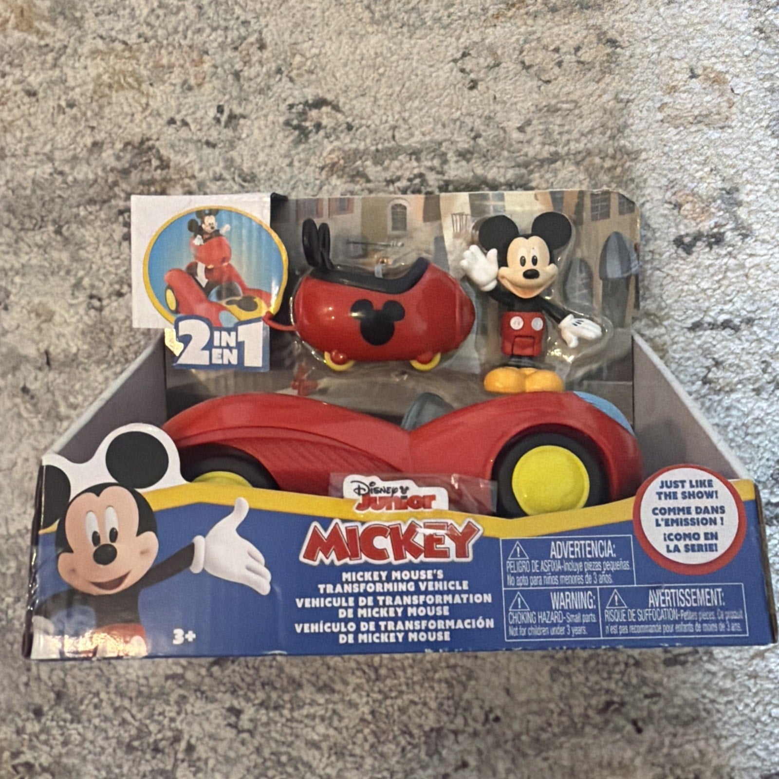 Disney Junior Mickey Mouse figure with red shorts and yellow shoes, packaged alongside a red and black car that transforms, displayed in branded box with colorful graphics.