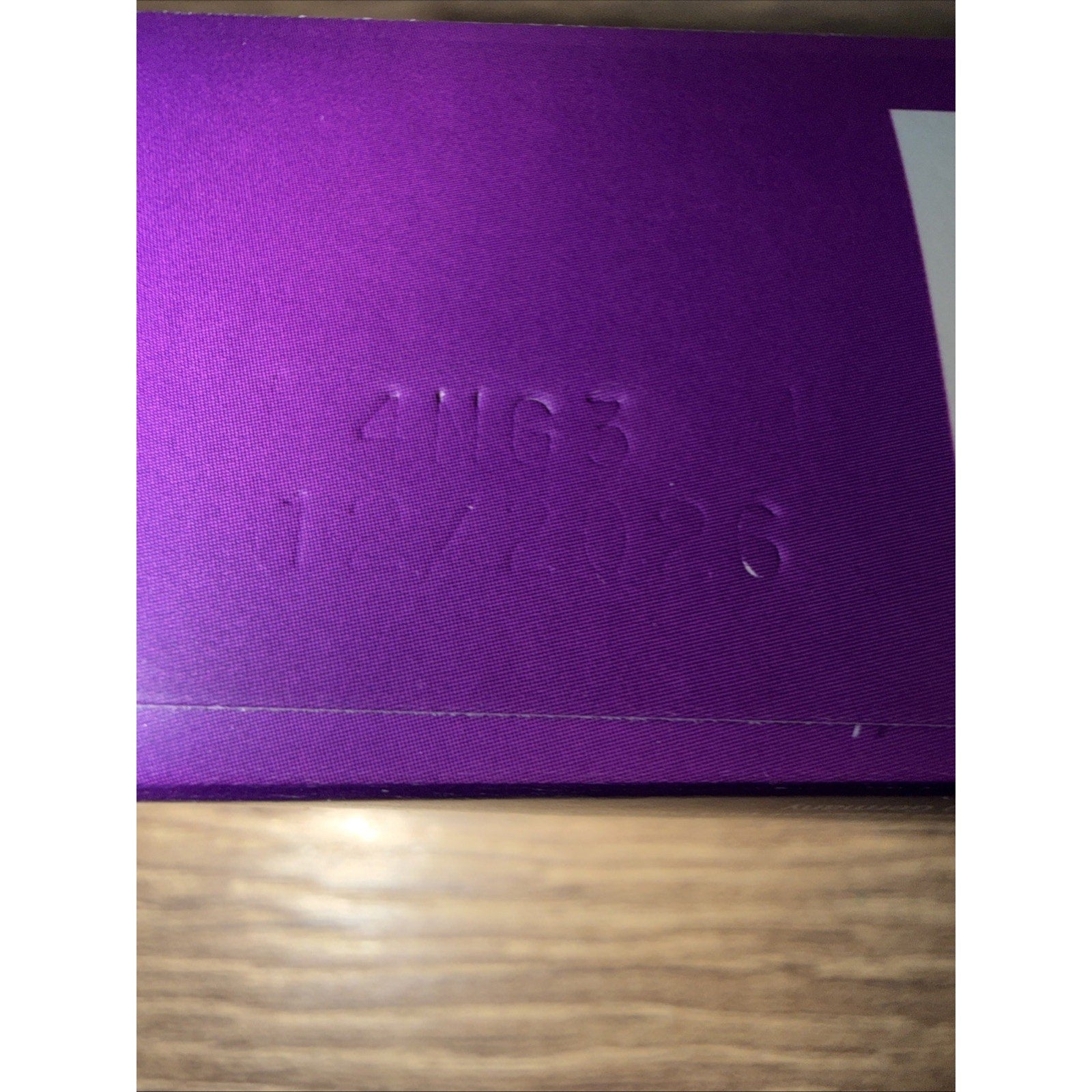 Close-up of a purple surface with an embossed code showing the numbers "21163" and "11/23026" above a wooden textured background.