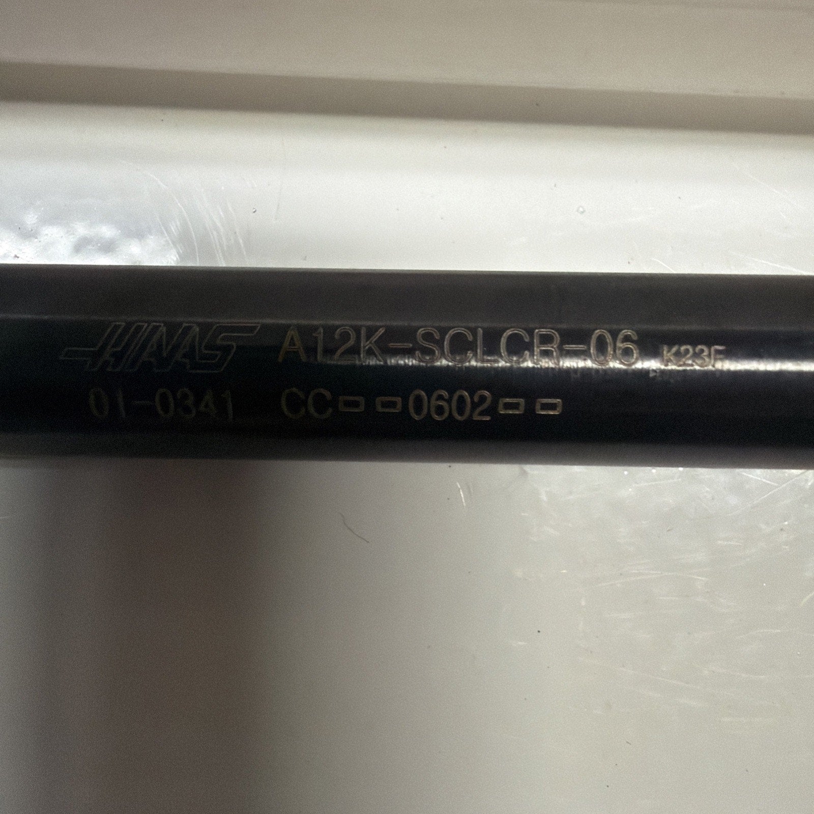 Close-up of a black cylindrical metal tool shaft with engraved alphanumeric codes and the brand name on a white reflective surface.