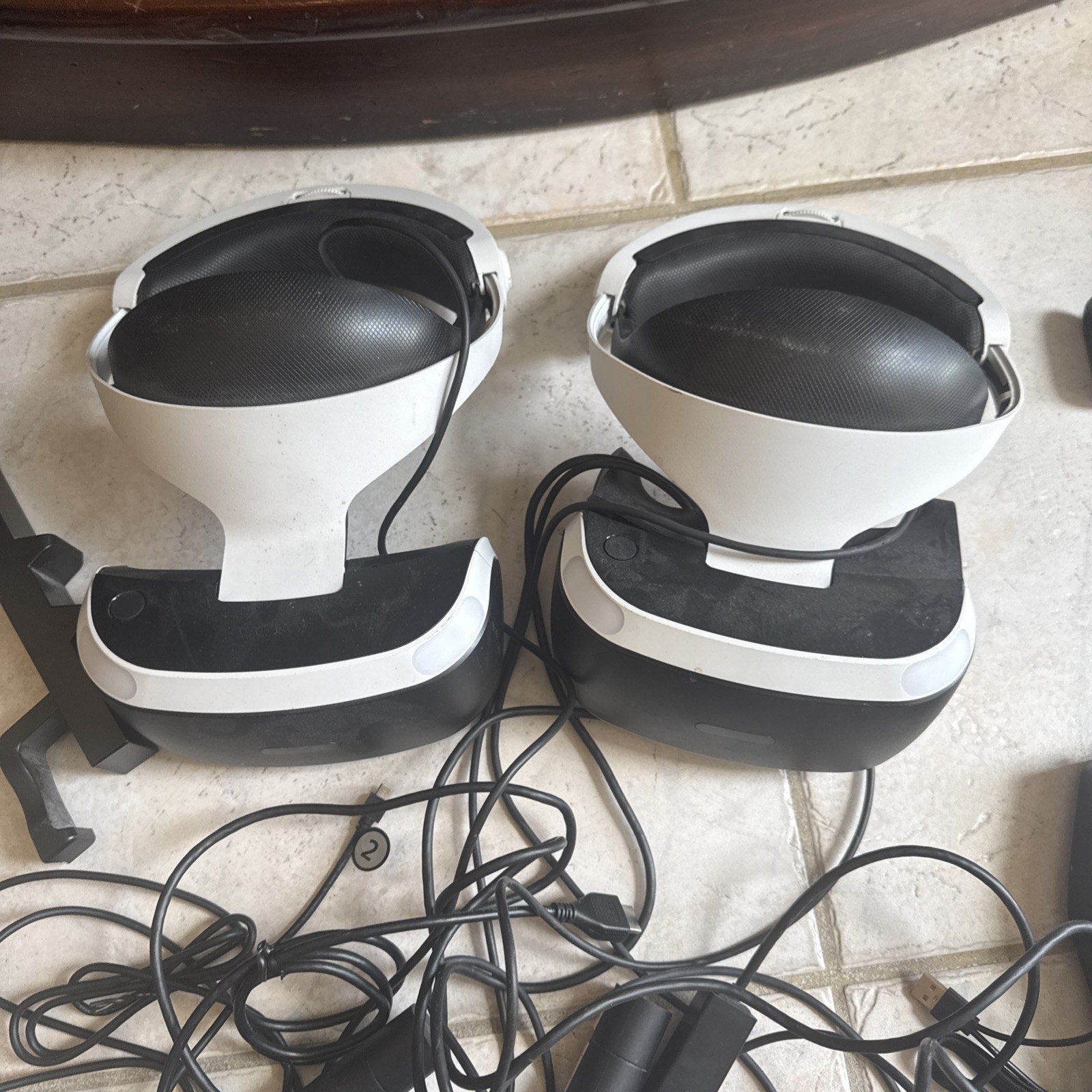 Two PlayStation VR headsets with attached cables and various additional accessories laid out on tile floor