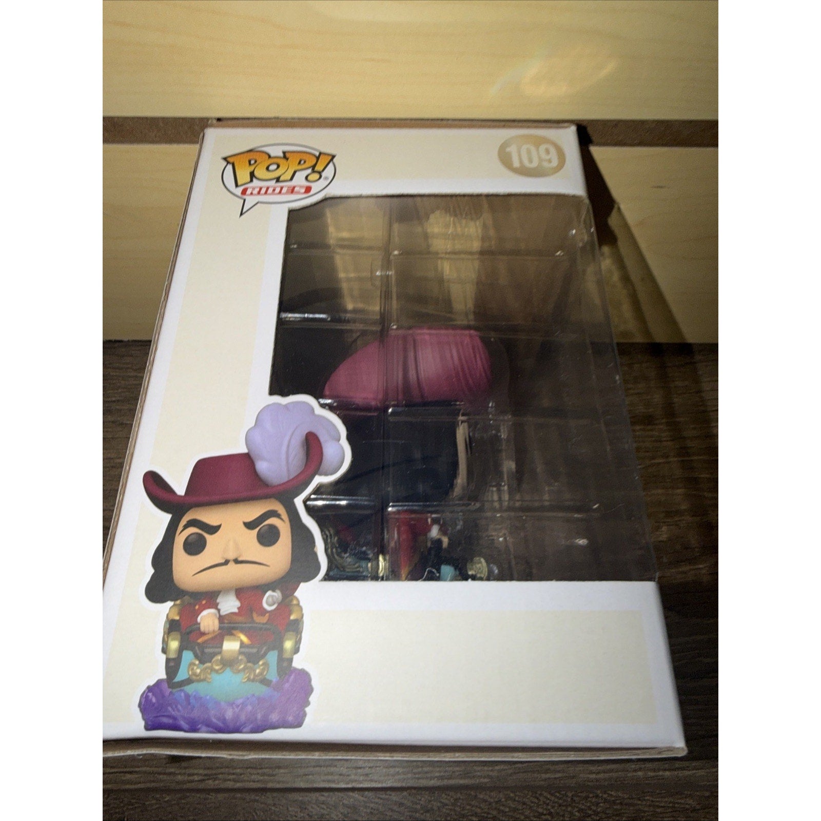 Funko Pop! vinyl figure in a white collectible box featuring a character wearing a red hat with a large feather, a red coat, and standing on a purple base with gold accents.