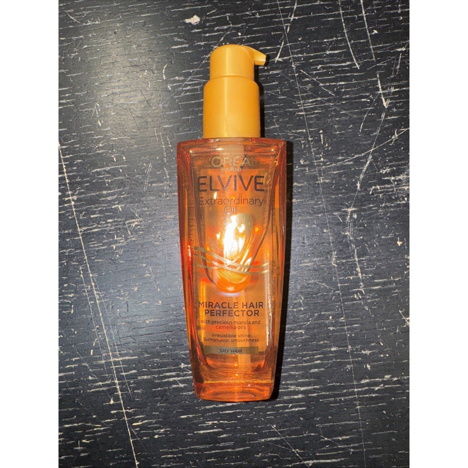 L'Oreal Elvive Extraordinary Oil Miracle Hair Perfector serum bottle with pump for dry hair on black scratched surface
