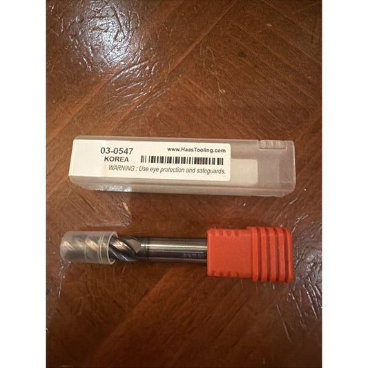 Metal cutting tool with a cylindrical shank and spiral flutes, partially covered in a clear plastic cap and red protective sleeve, placed on a wooden surface next to a white label-marked plastic storage box.