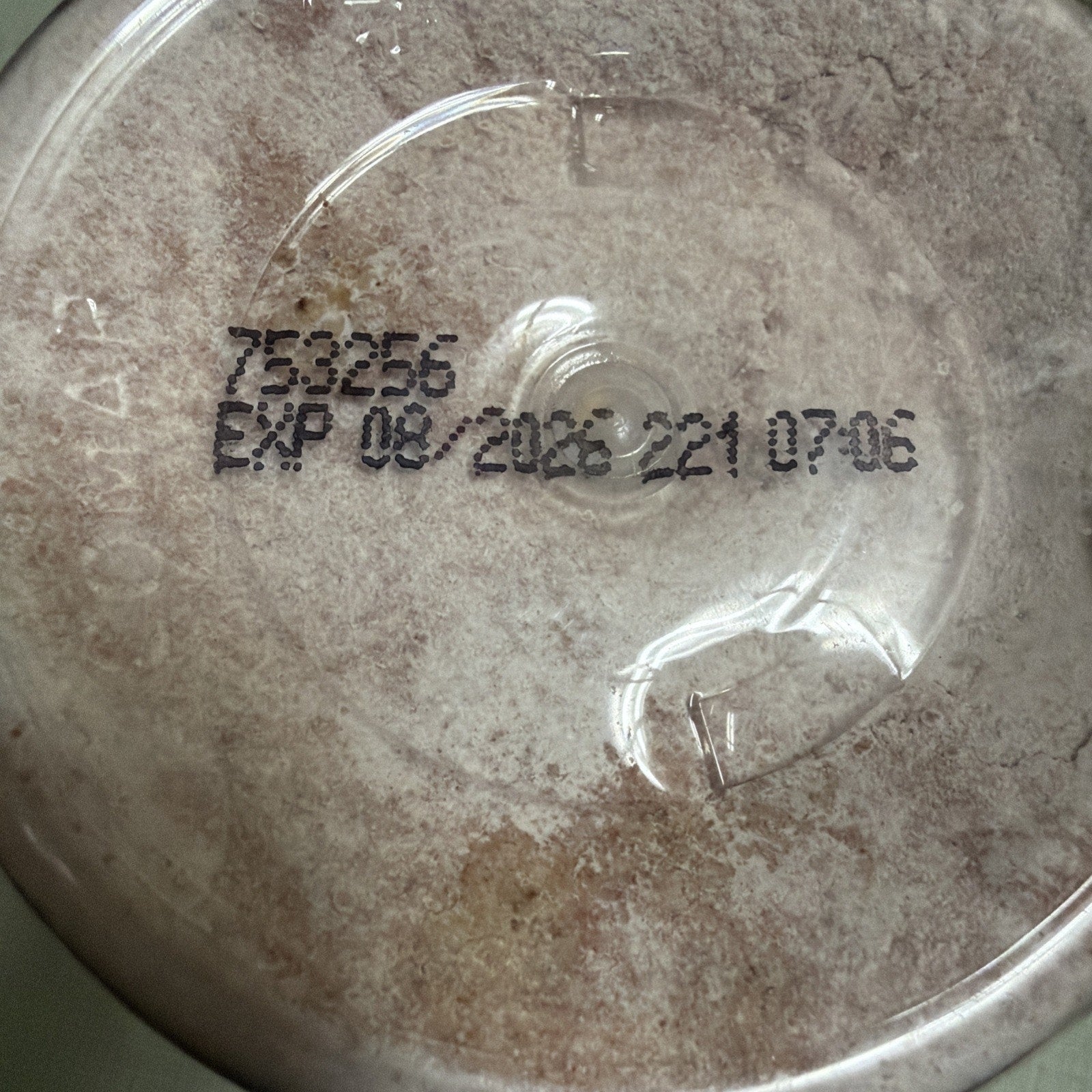 Close-up of the bottom of a container showing a printed expiration date of 08/2028 and batch number 753256 on a slightly textured, translucent surface.