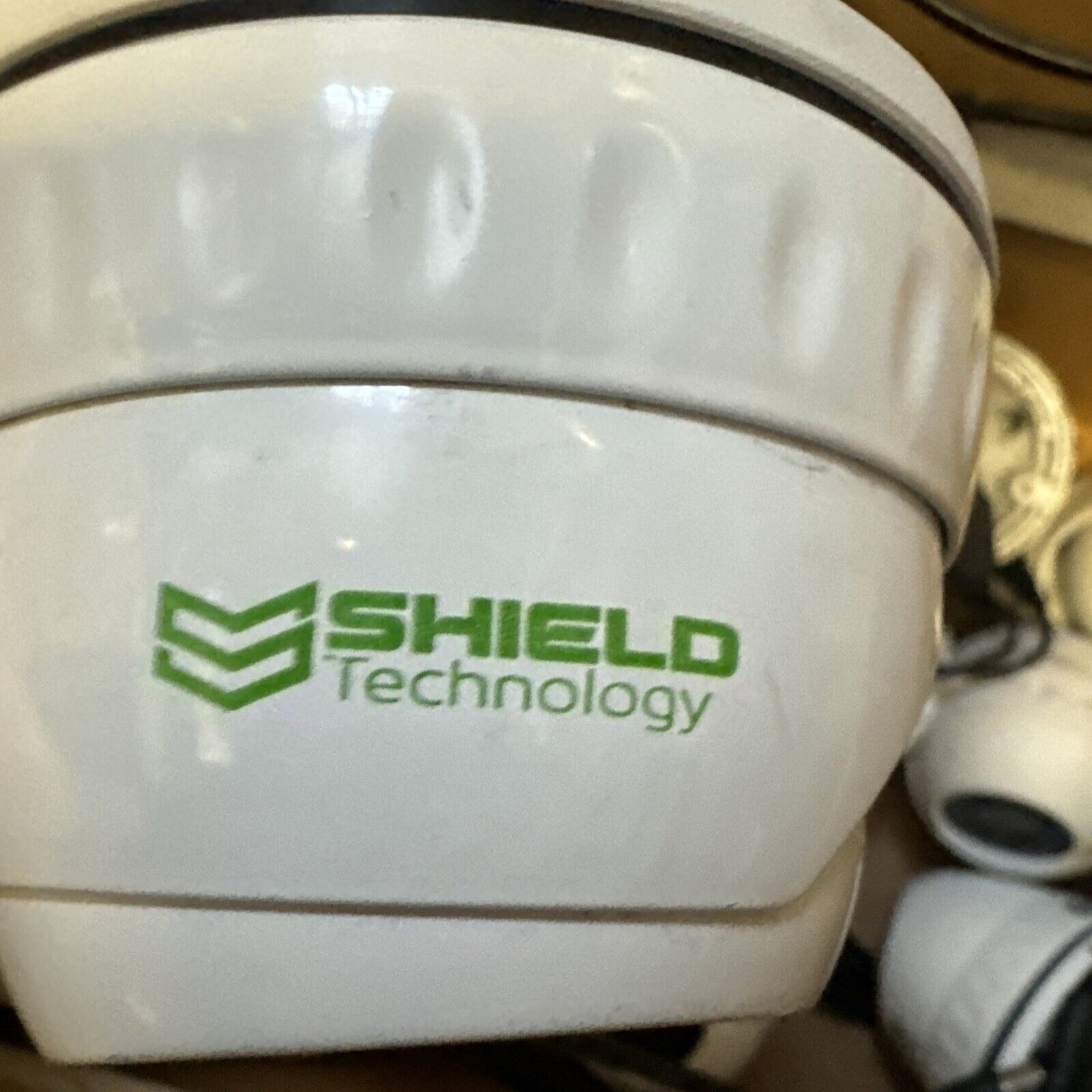 White analog CCTV dome camera with Shield Technology logo printed on the side showing security device close-up