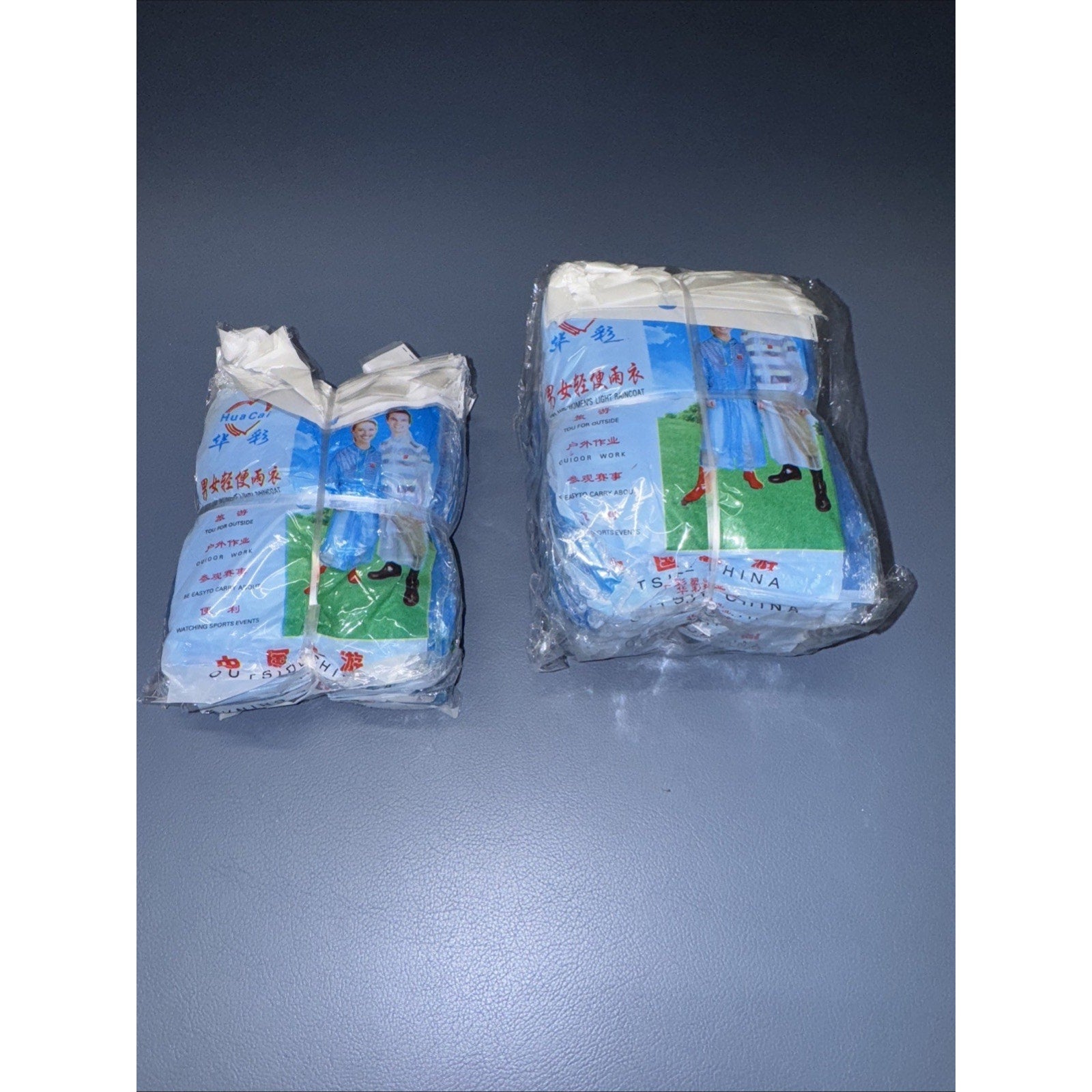 Two sealed packs of waterproof light ponchos for men and women displayed on gray surface with blue and green packaging