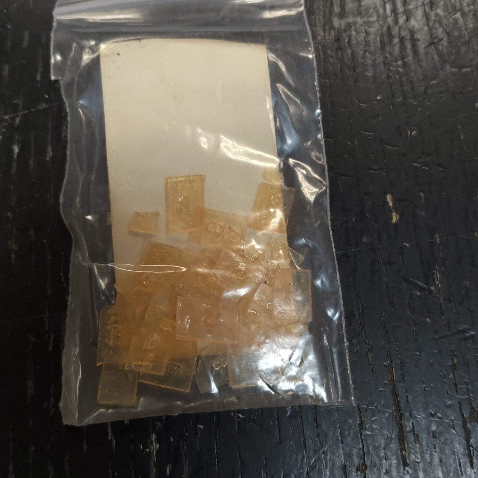 Small translucent amber-colored plastic clips or pieces contained inside a clear resealable plastic bag placed on a dark textured surface.