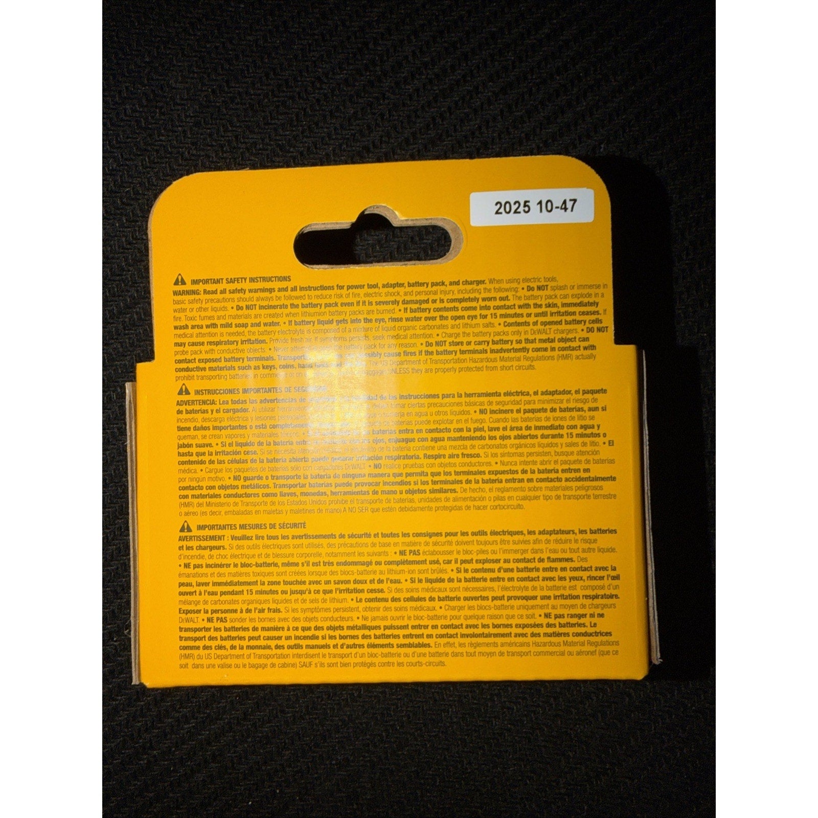 Yellow rectangular product packaging with detailed safety warnings and instructions printed in several languages and a small white sticker displaying the code 2025 10-47, set against a black textured background.