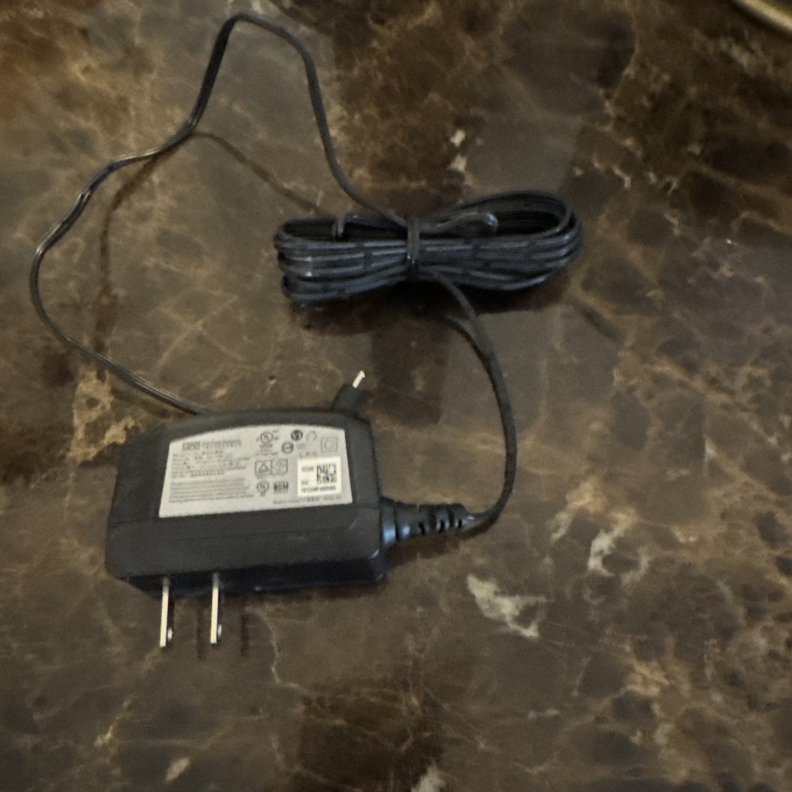 Power supply adapter for ADT RC8025 security camera with plug and attached power cable on marble surface